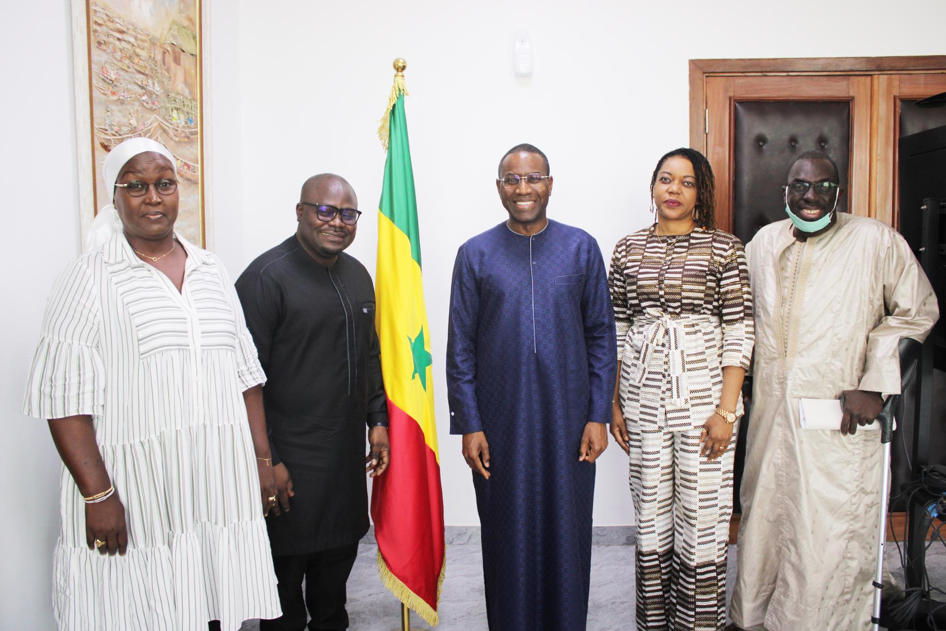Groupe de 5 personnes dont deux femmes devant le drapeau du Sénégal