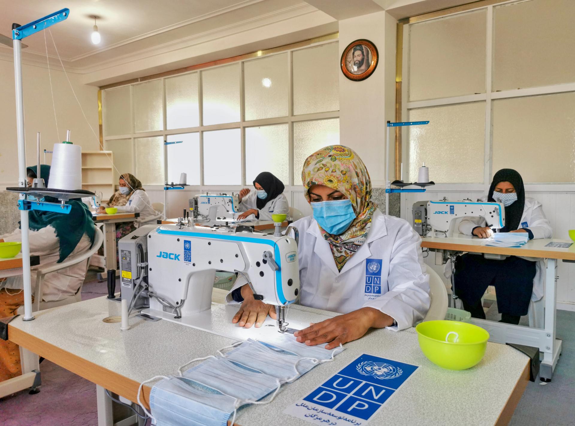 A photo of several women in lab coats and face masks making face masks in a UNDP workshop in Iran.
