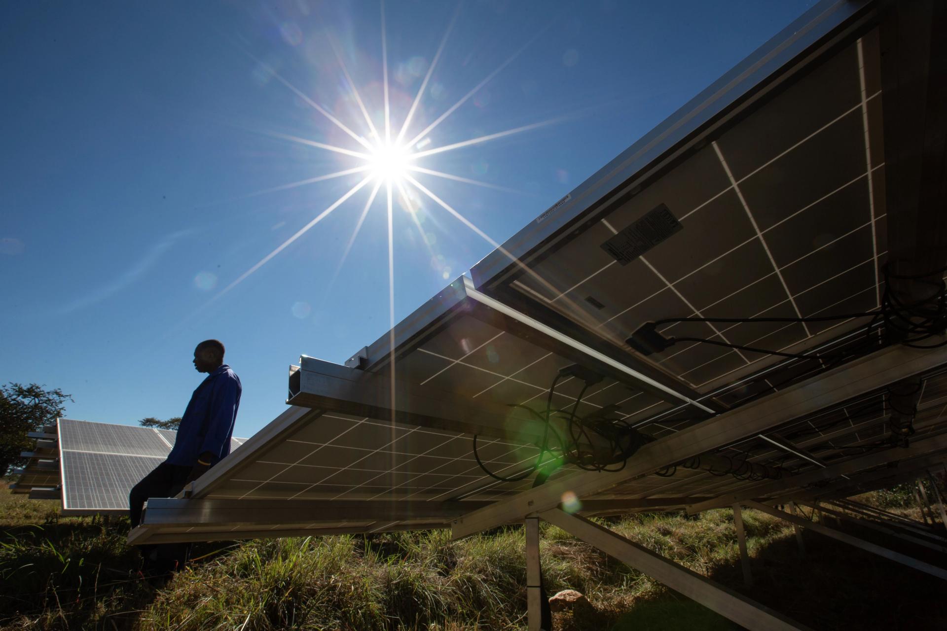 Silhouette of a man working on solar panels against a sunny blue sky.