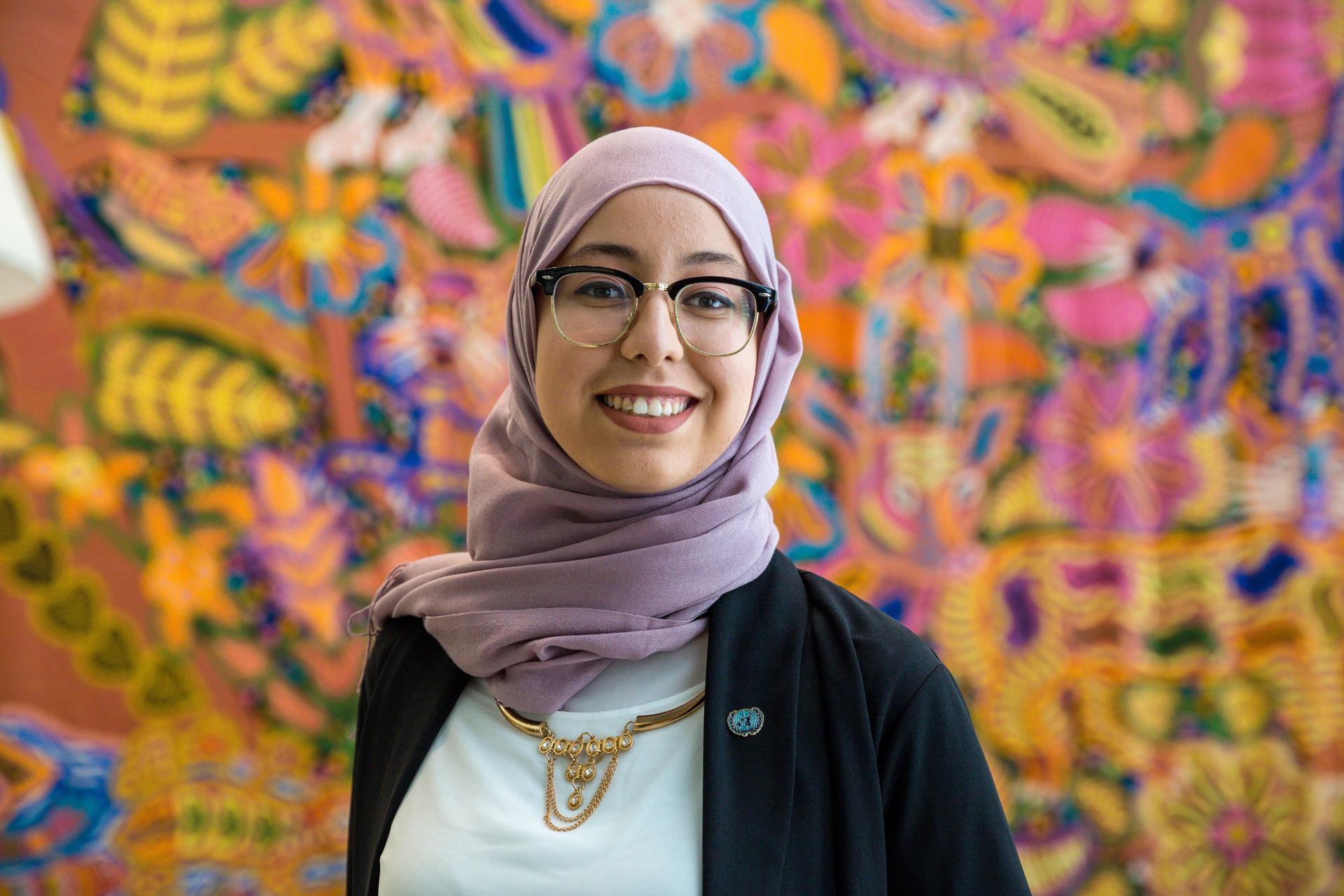 A young woman poses in front of a colourful background