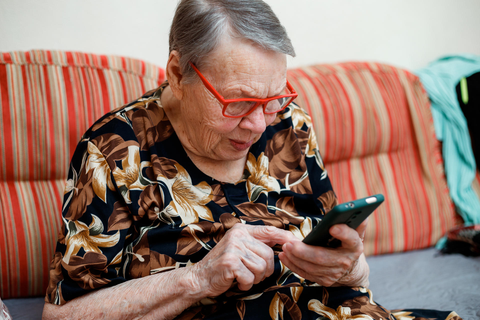 A grey-haired women presumably over 80 is looking at and pointing with her finger at a mobile phone