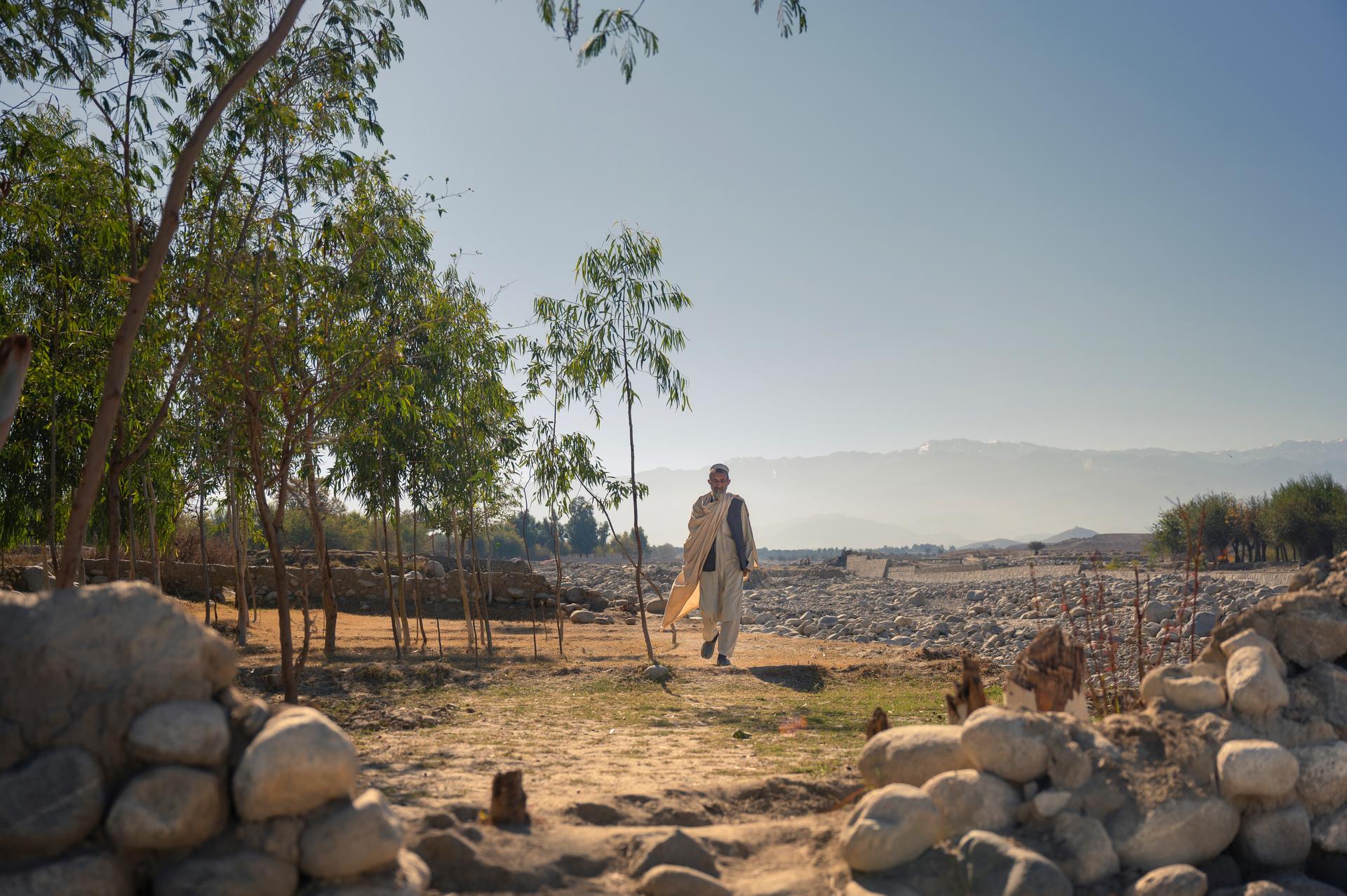 A man walking across a landscape with mountains in the distance
