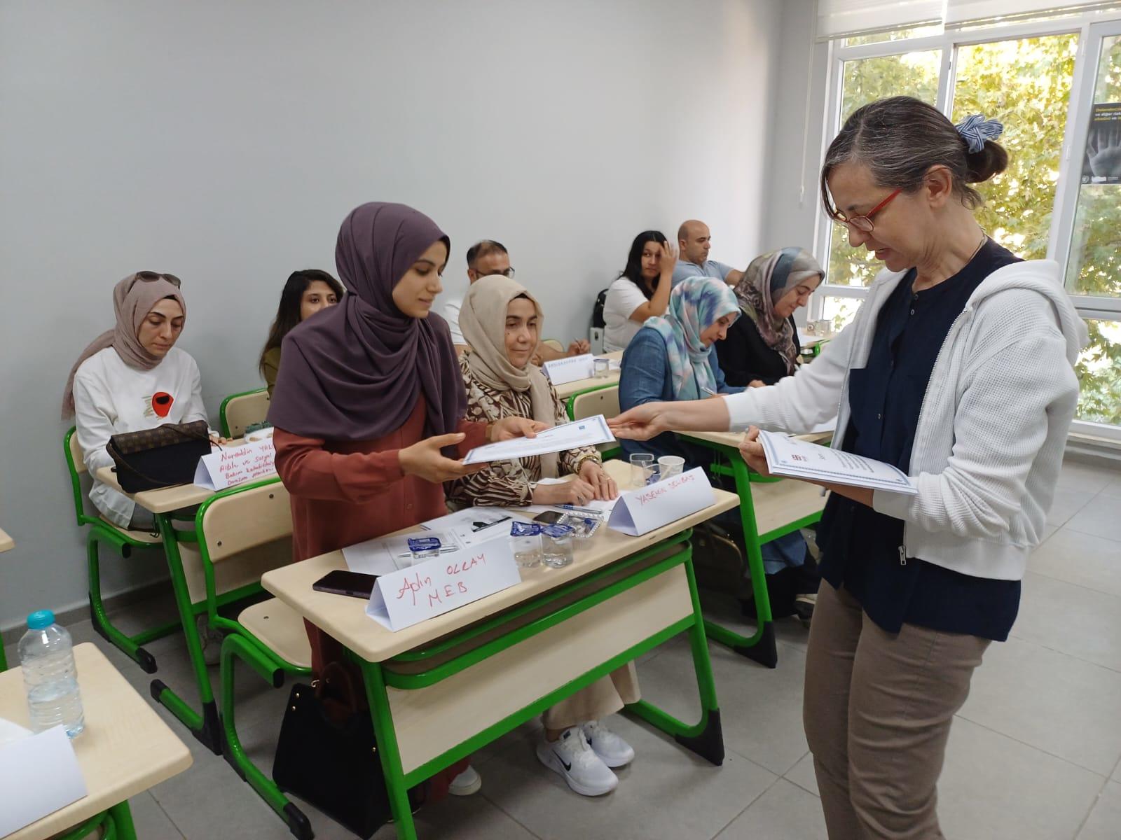 8 women sitting in school desks with one standing and receiving a certificate from a female instructor