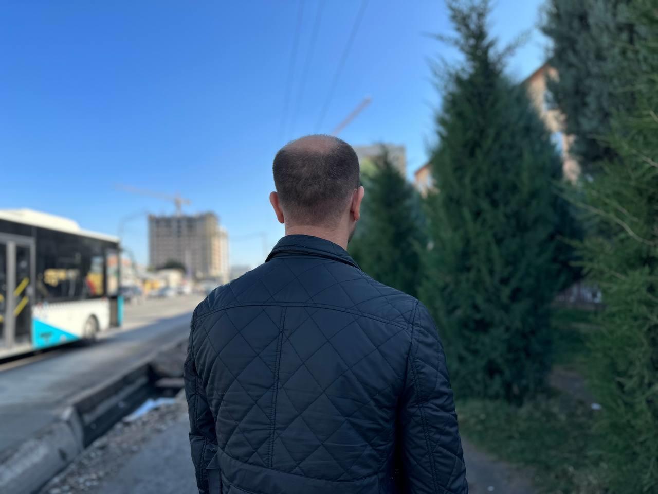 A view from behind of a man, likely middle-aged, standing on a sidewalk in Dushanbe, Tajikistan.