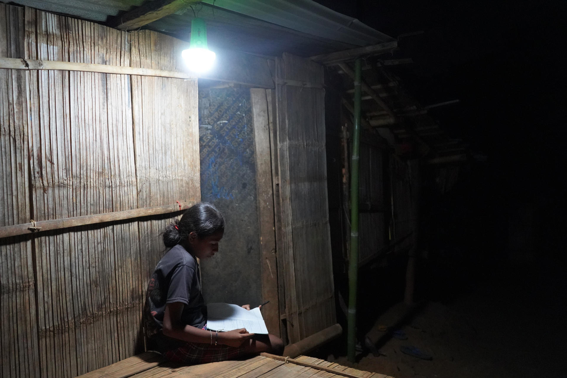 A girl studies under a lamp outside in the dark on a rural village of Timor-Leste