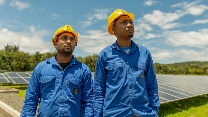 Men in hard hats and overalls stand next to solar panels