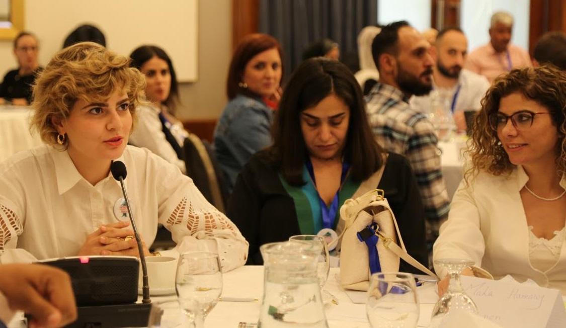 Yara Haydar speaking into a microphone in a room full of people