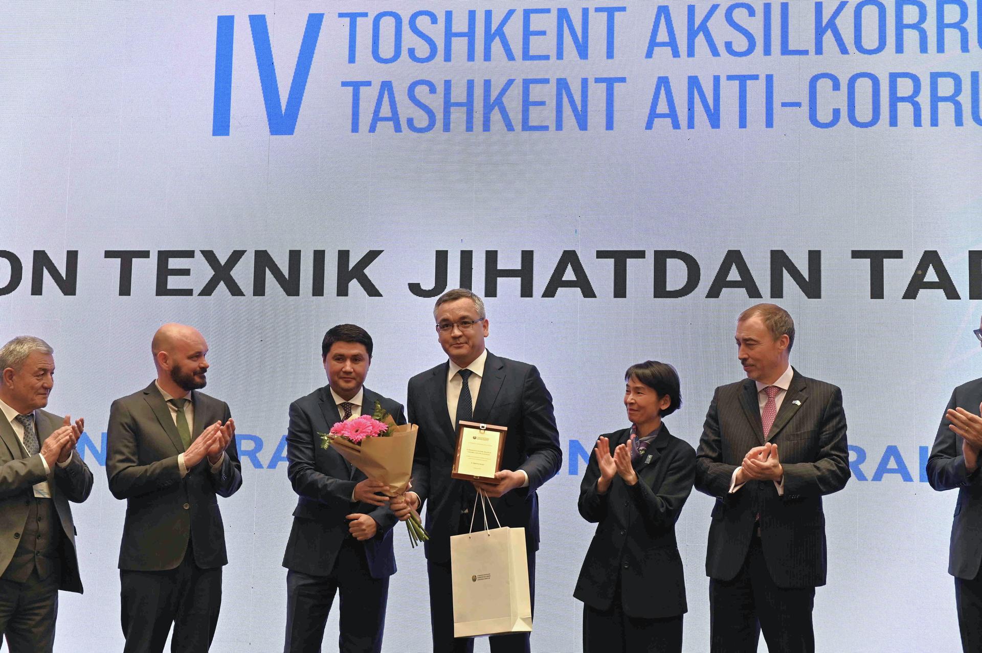 Group of people holding award and flower bouquet at the stage
