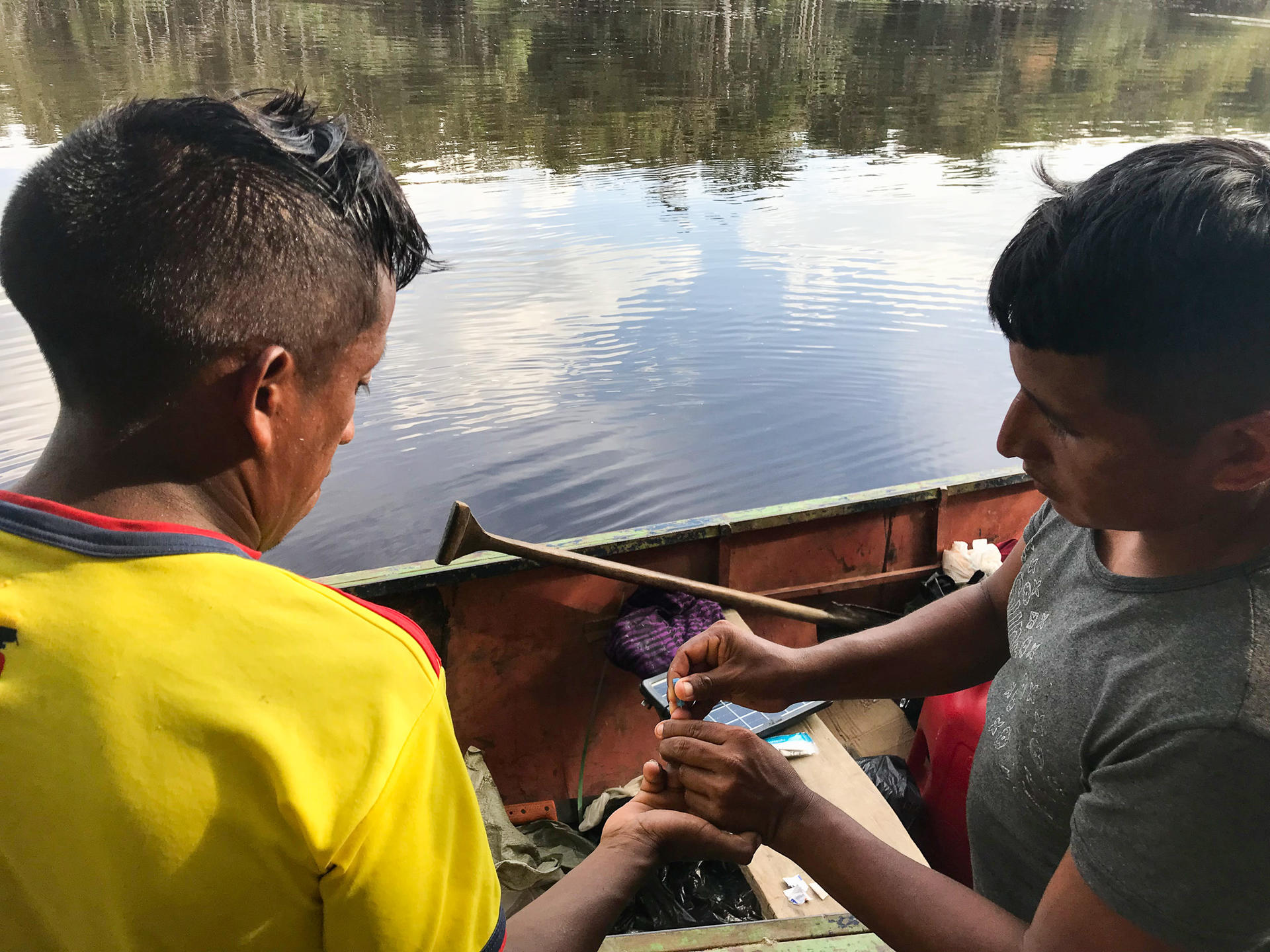 Dos hombres sentado en un bote en el agua haciéndose pruebas rápidas de malaria