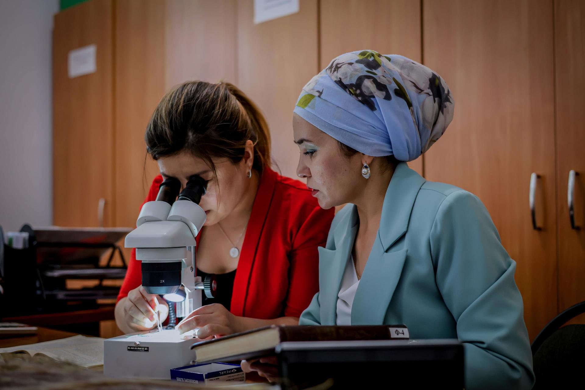 two women biologists in front of the desk with microscope and books