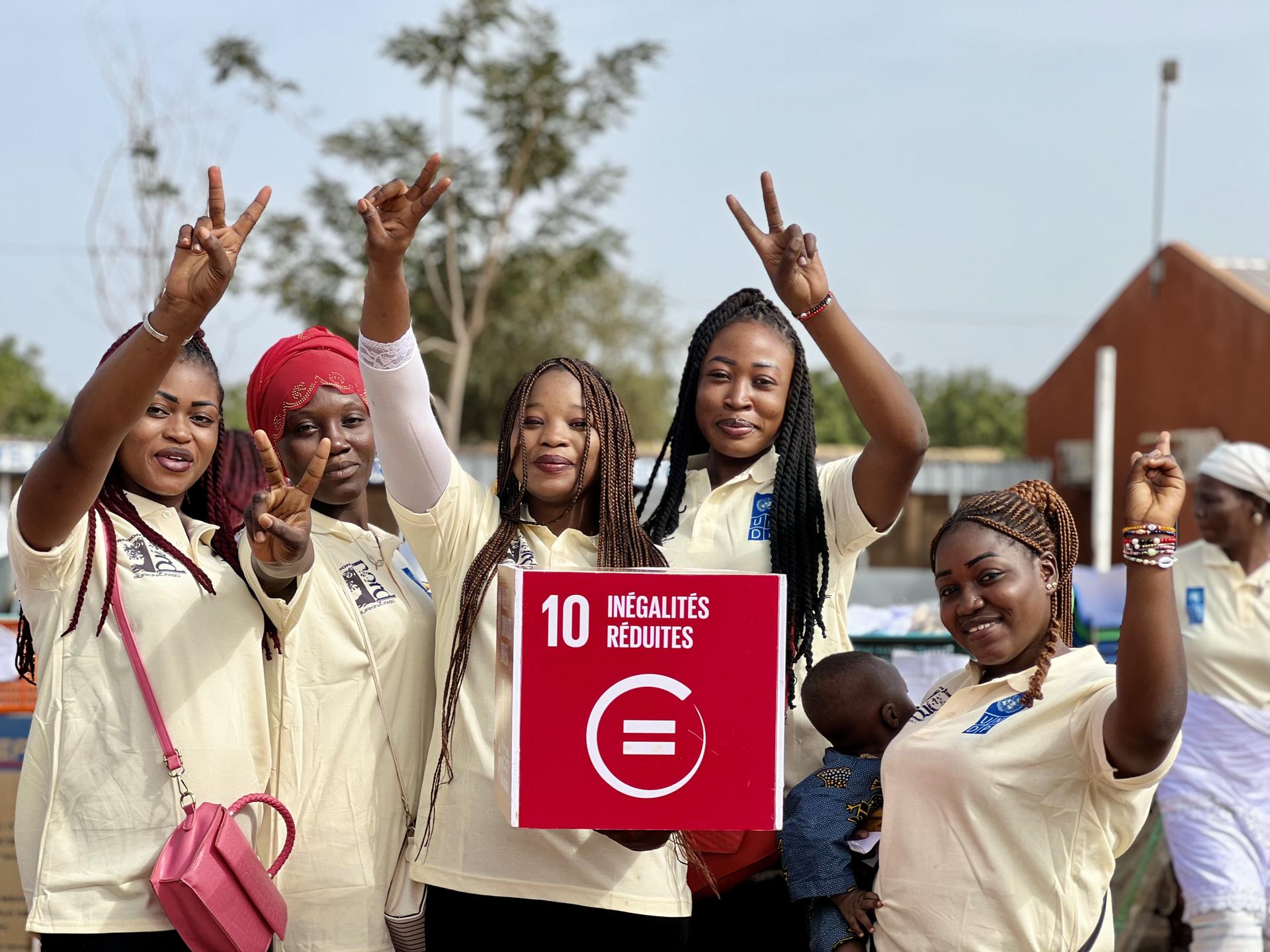 Women flashing peace signs and holding up an SDG sign for reduced inequalities