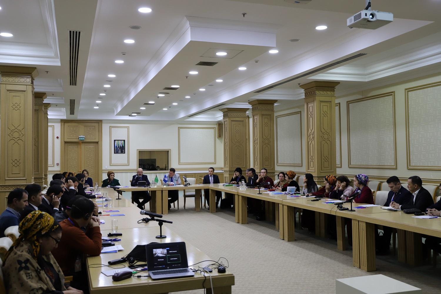 A large meeting room with people seated around a long table, engaged in discussion.