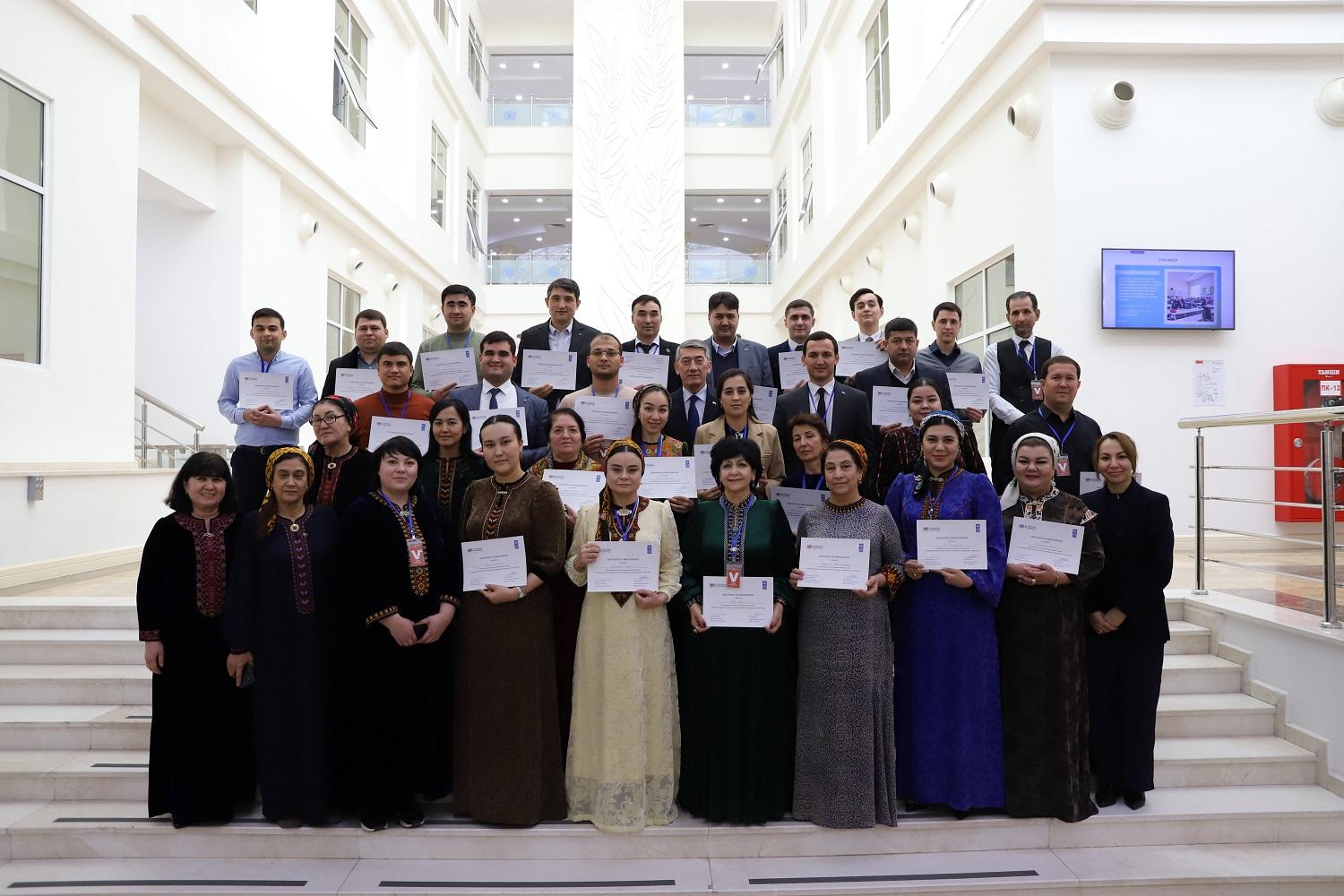 A diverse group of people stands together, holding certificates in a bright, modern space.