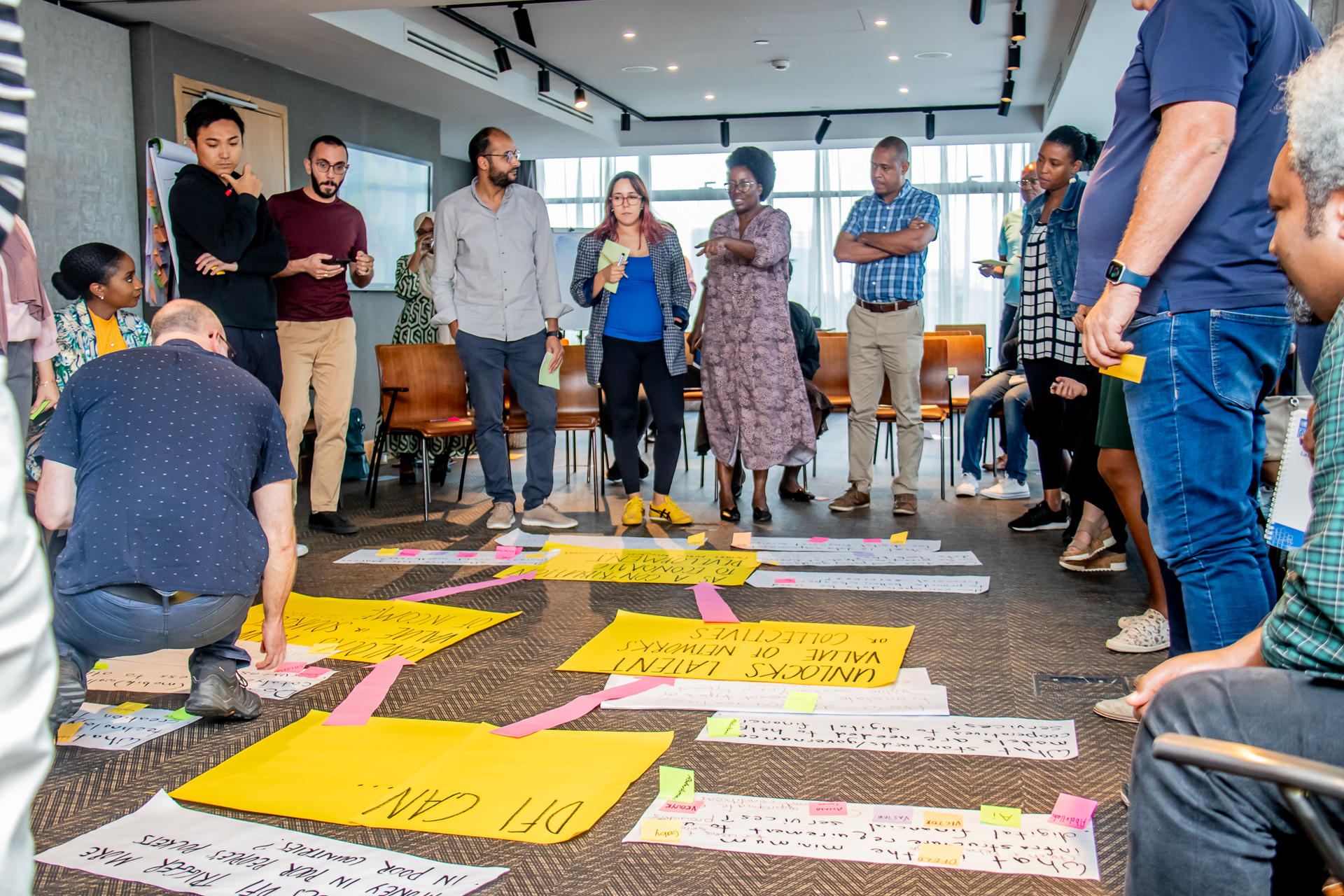 a group of people standing around large papers on the floor - group work
