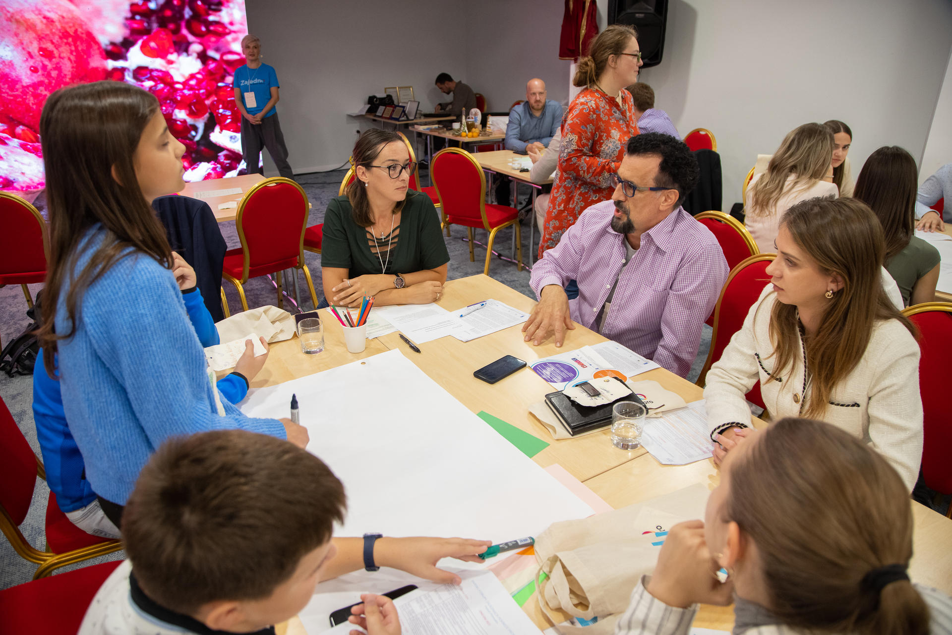 Group of diverse people engaging in discussion around a table in a vibrant, well-lit room.