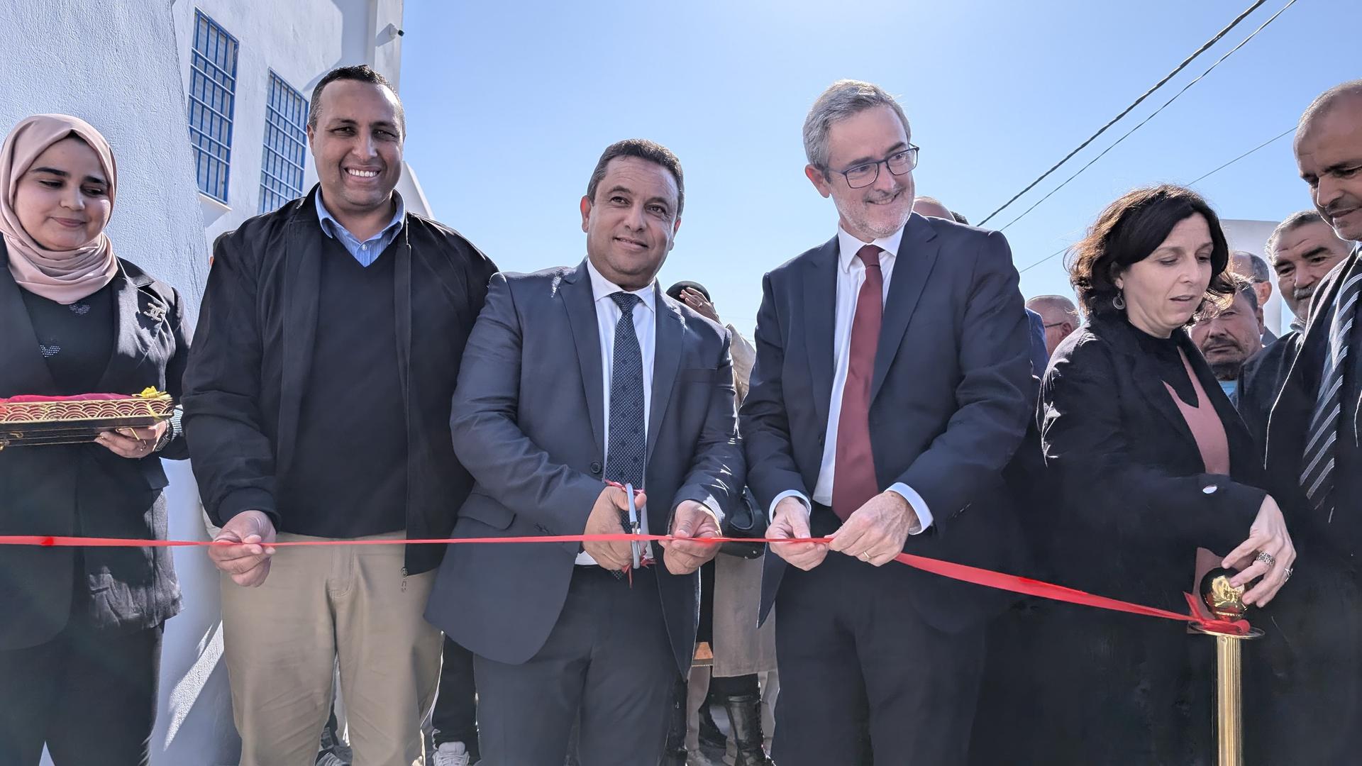 Group of people cutting a ribbon outside a building, smiling and celebrating.