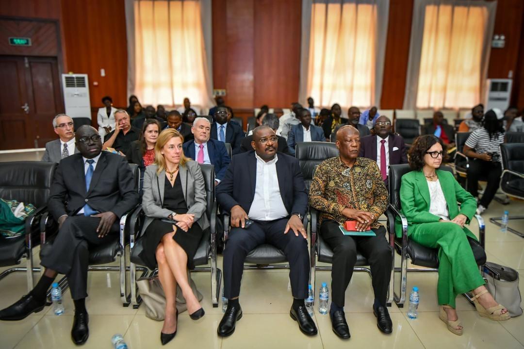 A diverse group of people seated in a formal setting, with various expressions and attire.