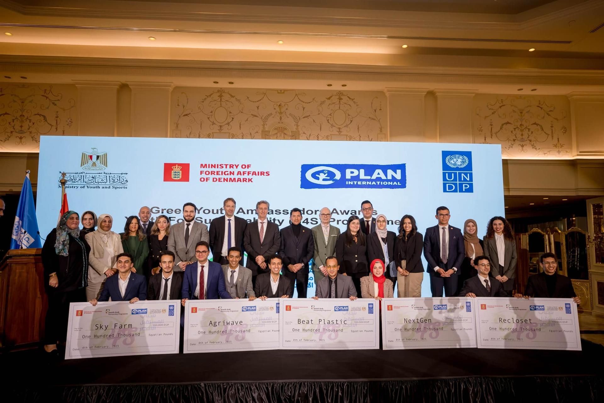 Group of people posing in front of a backdrop, holding large checks at a ceremony.