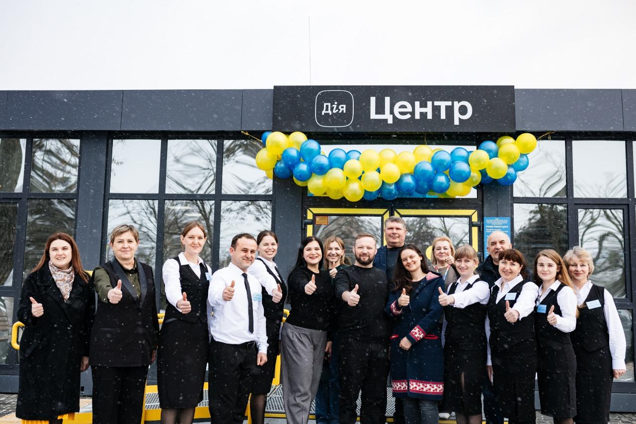 A group of smiling employees in formal attire, giving thumbs up in front of a building.