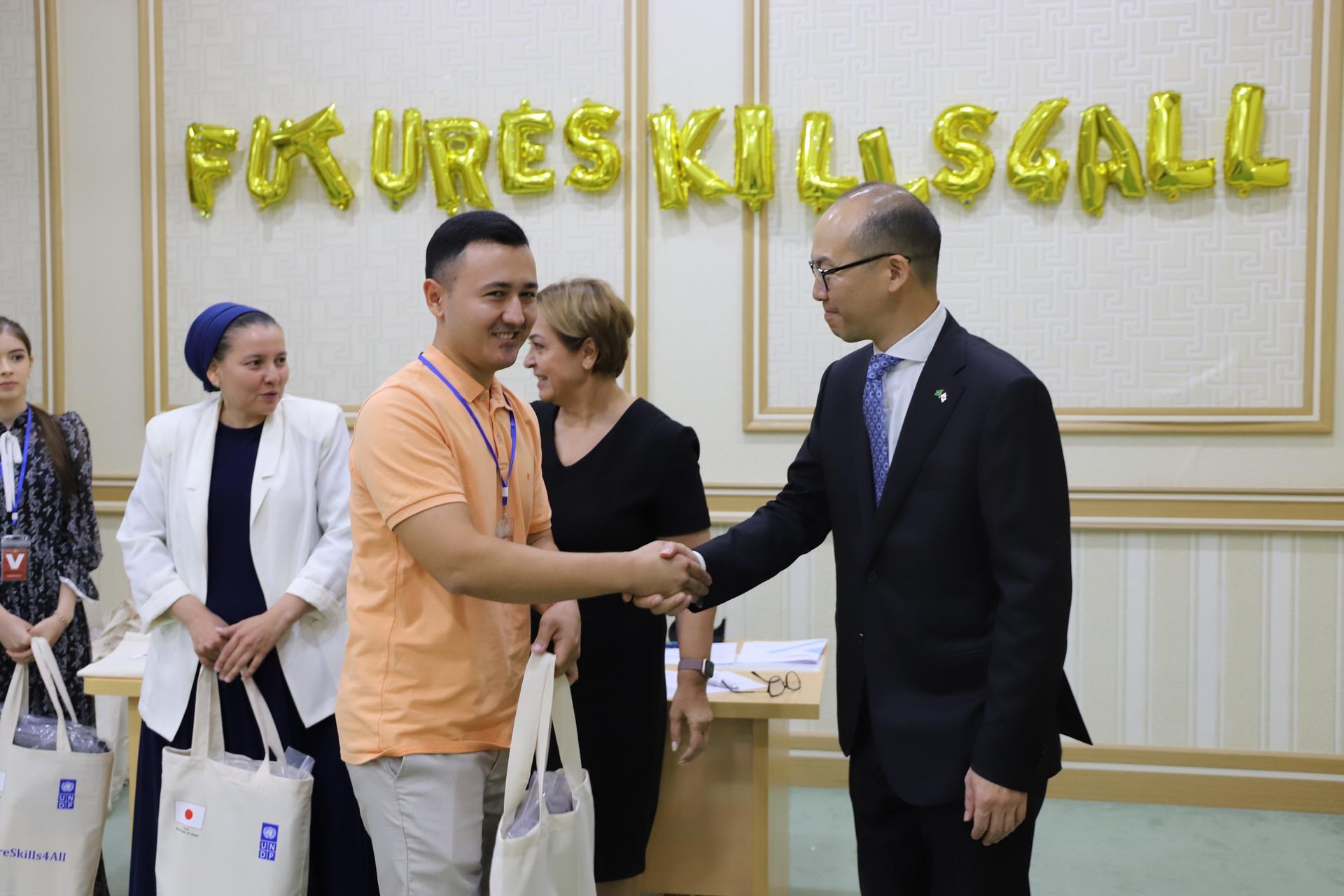 A formal handshake between two men, with others looking on; gold balloons spelling "FUTURES KILLS CALL."