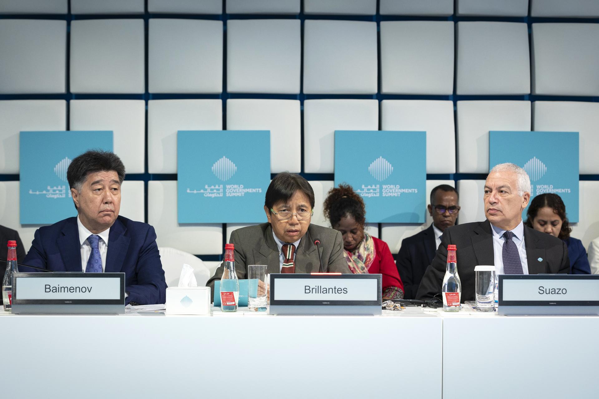 Five people seated at a conference table, discussing with blue background panels.