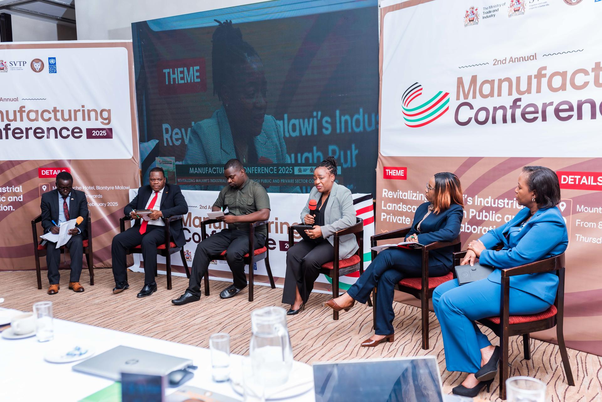 Panel discussion at a manufacturing conference with five speakers seated on stage.