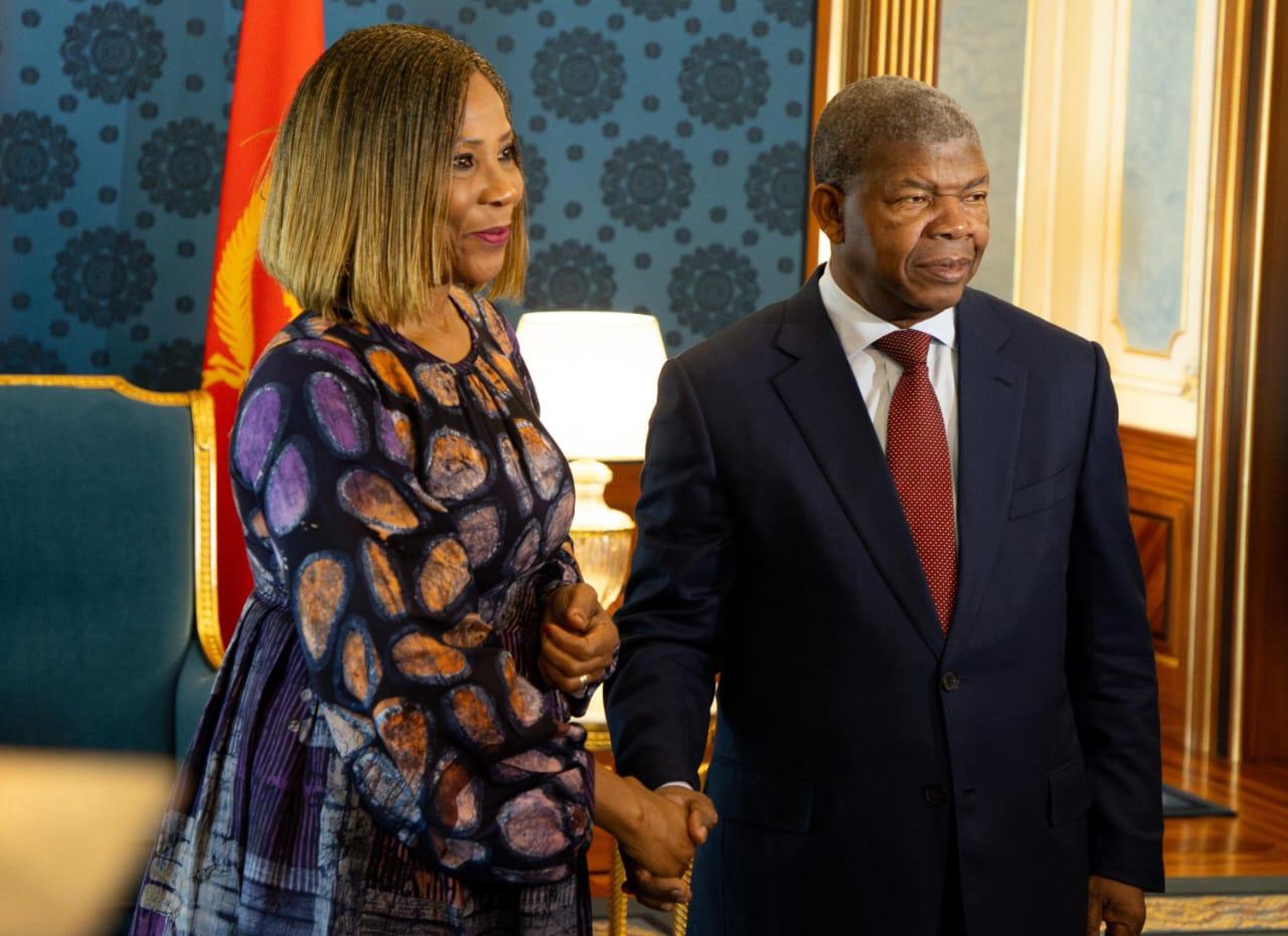 A woman and a man shake hands in a formal setting, both wearing elegant attire.