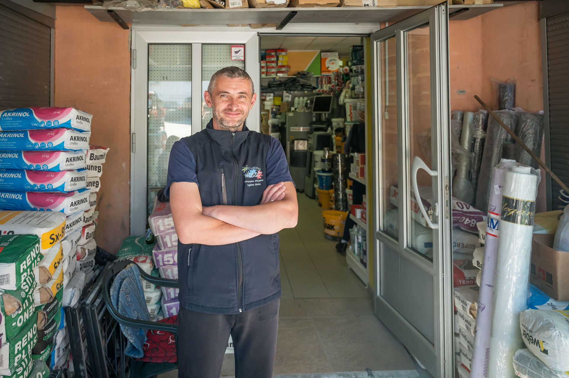 A man stands confidently at the entrance of a store filled with supplies and tools.