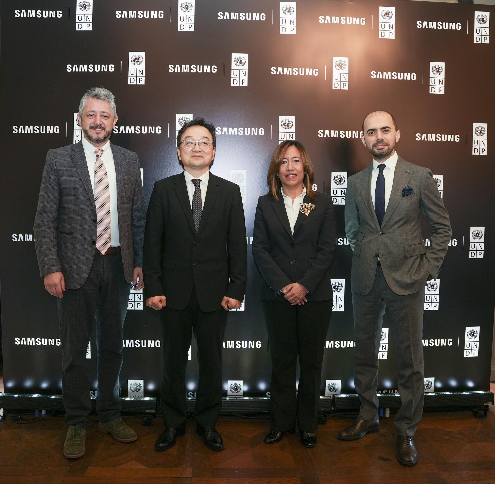 Four professionals in formal attire standing together against a branded backdrop.