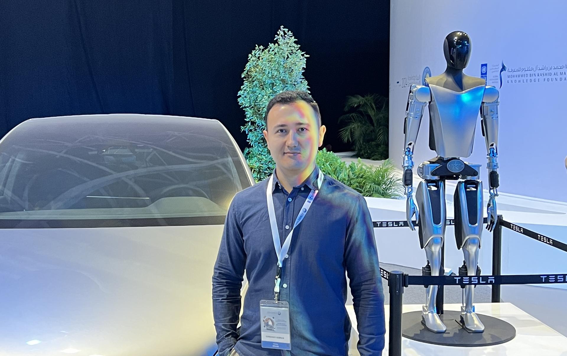 A man stands beside a futuristic car and a humanoid robot in an exhibition setting.