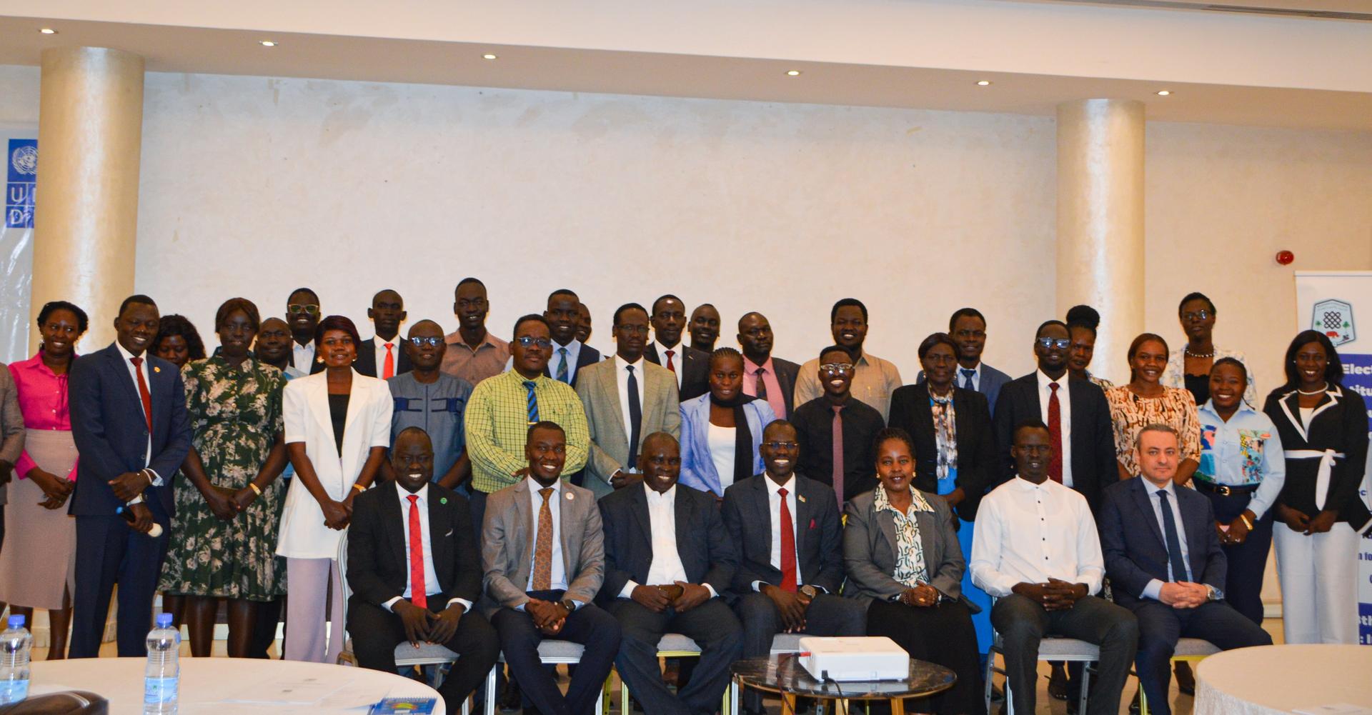 Group photo of diverse individuals in formal attire, standing together in a conference room.