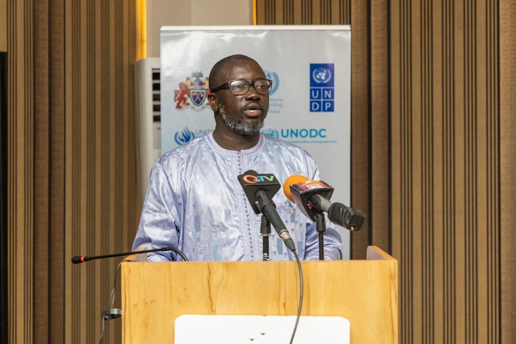 A man in a traditional outfit speaks at a podium with microphones in a conference setting.