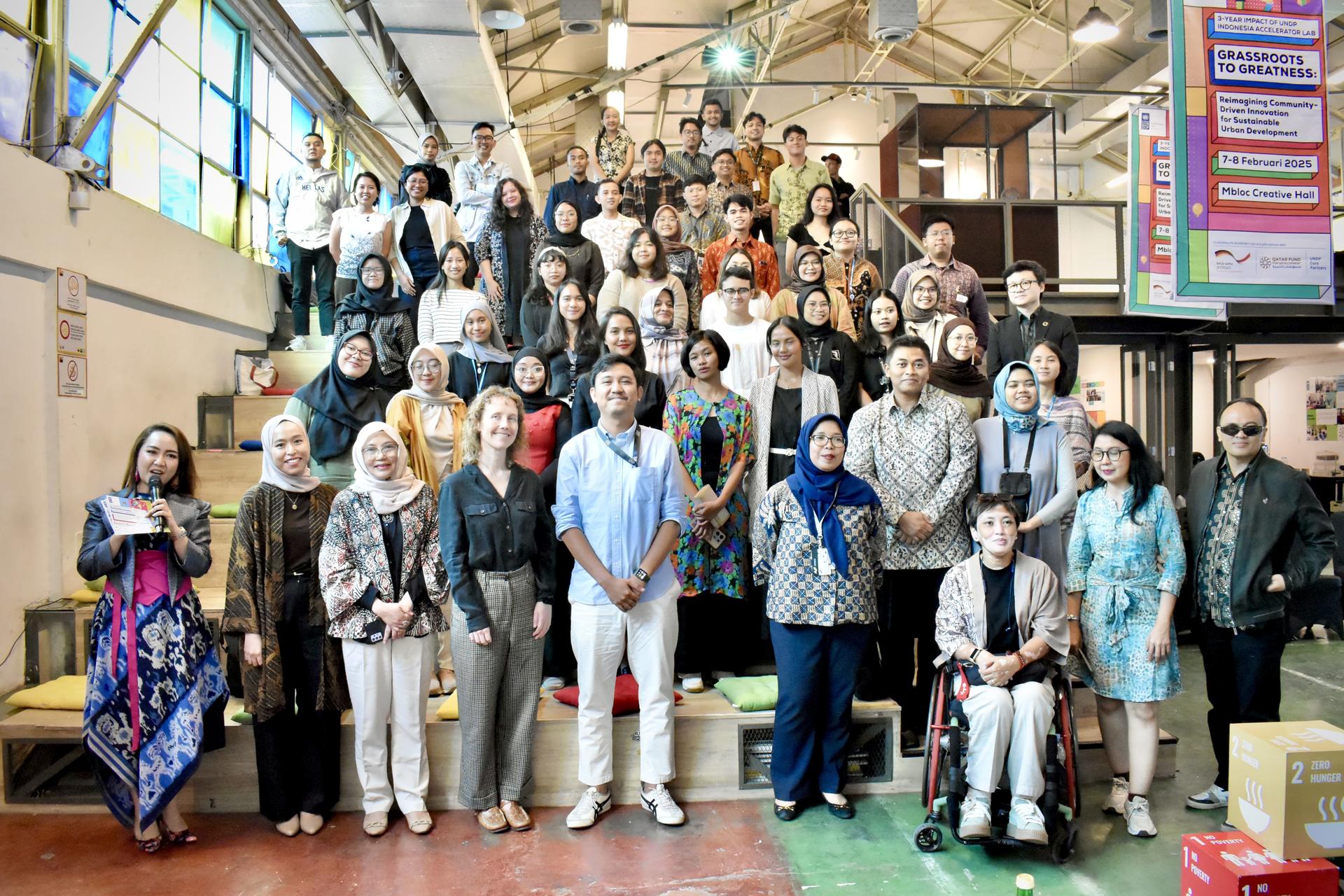 A large diverse group of people posing together on stairs in a colorful industrial space.