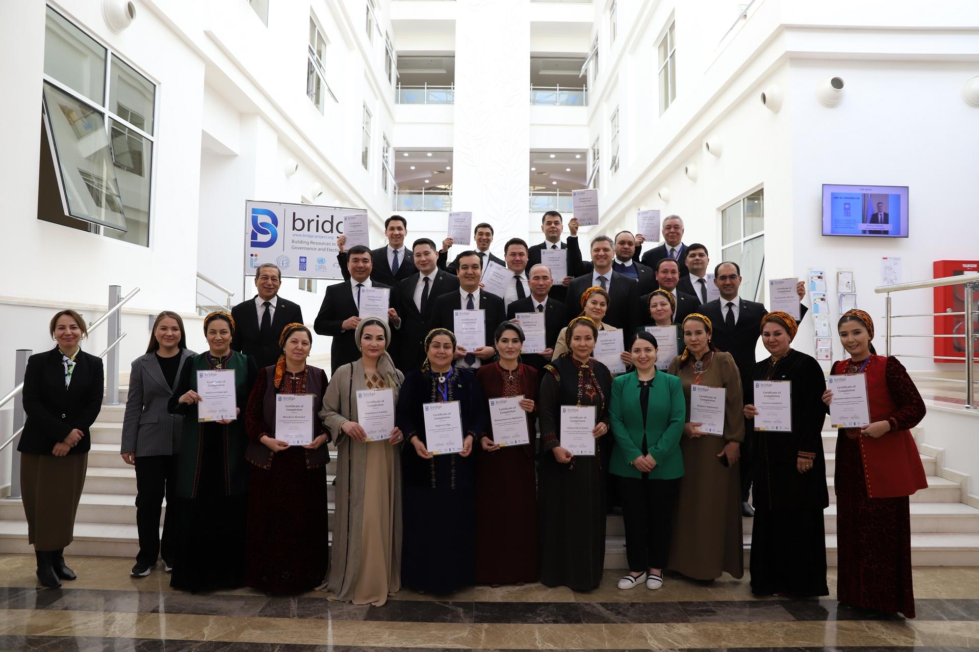 Group photo of diverse individuals holding certificates in a bright, modern building.