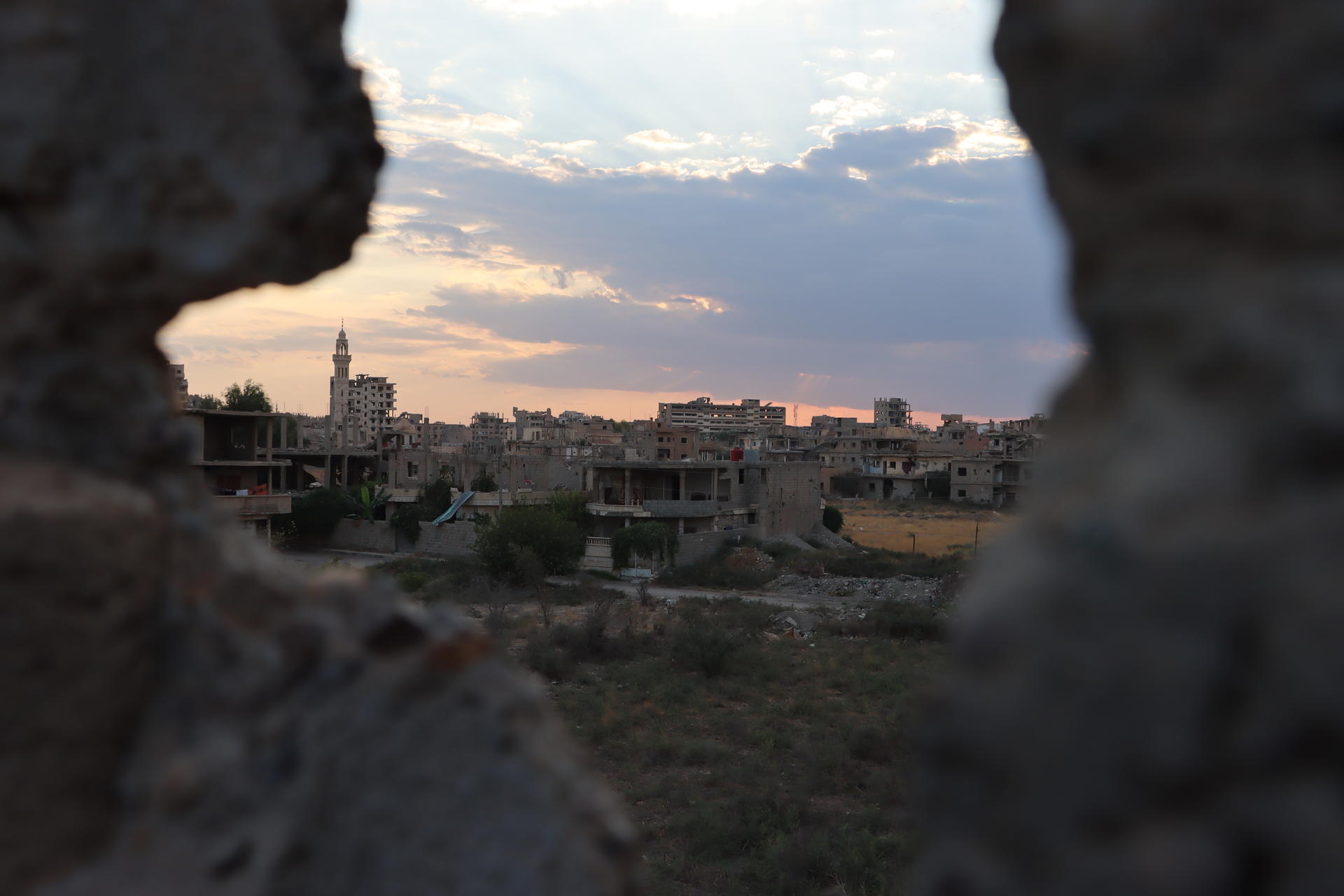 View of a ruined landscape at sunset, framed by a hole in a wall.
