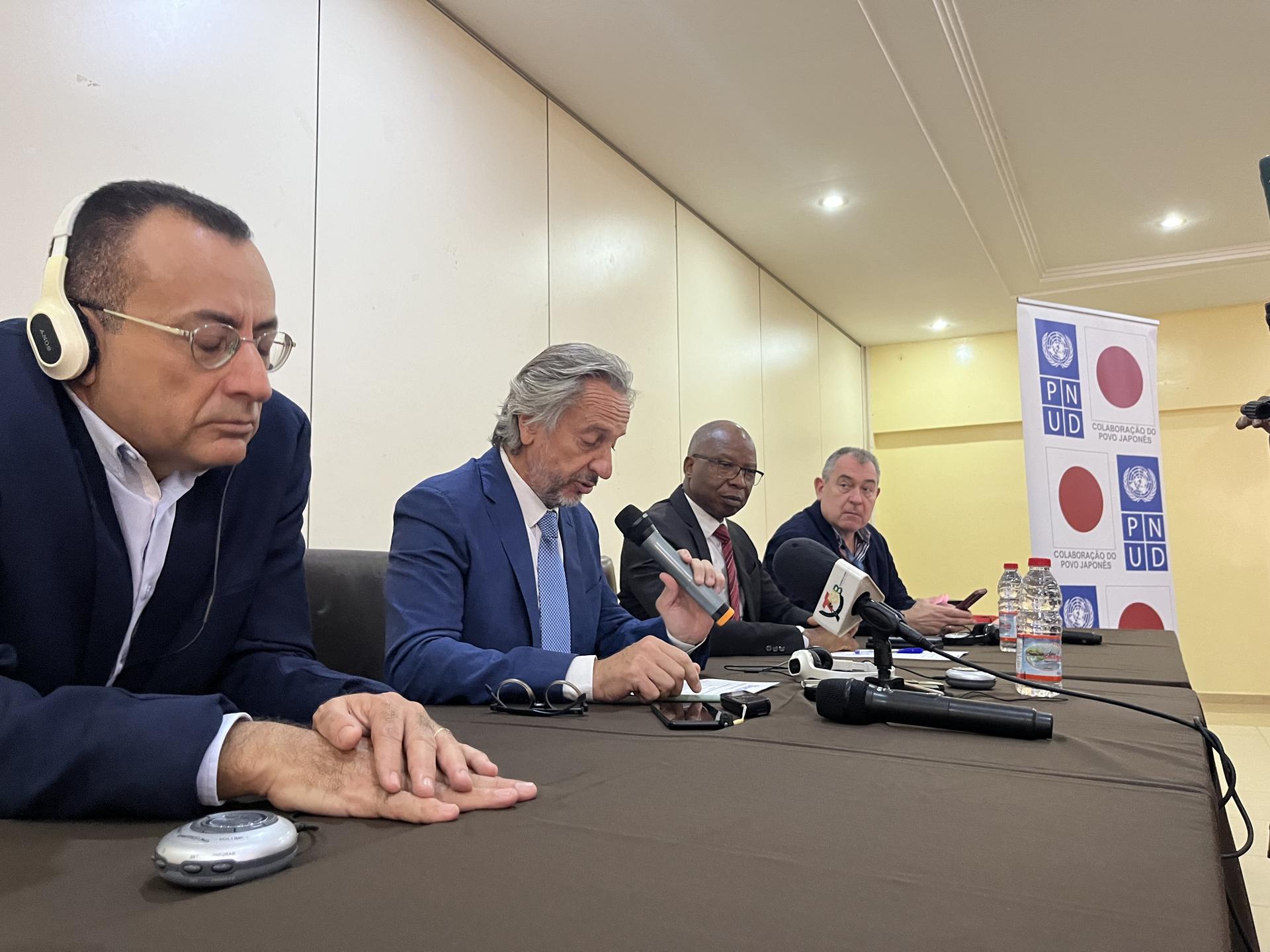 Four men seated at a table with microphones, engaged in a discussion or conference setting.