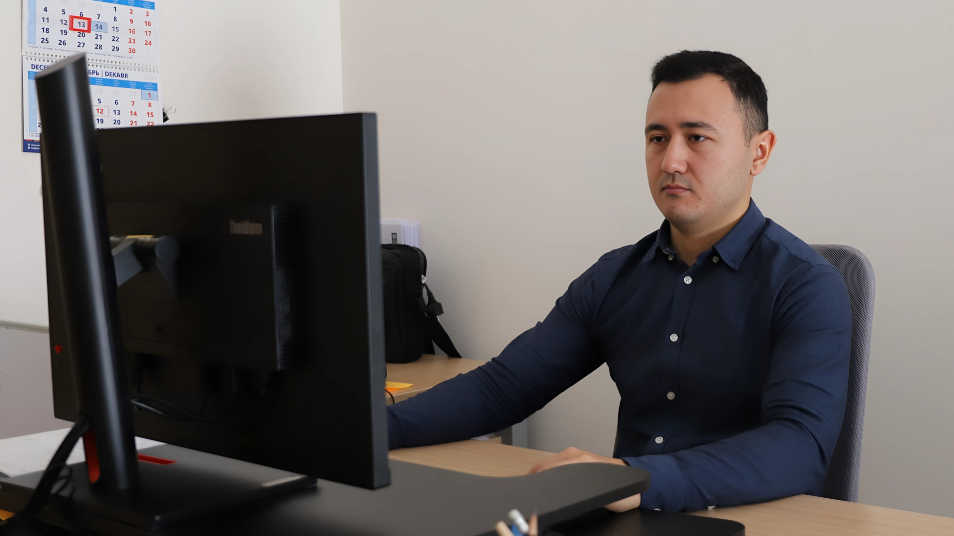 A man in a blue shirt sits at a desk, focused on a computer screen.