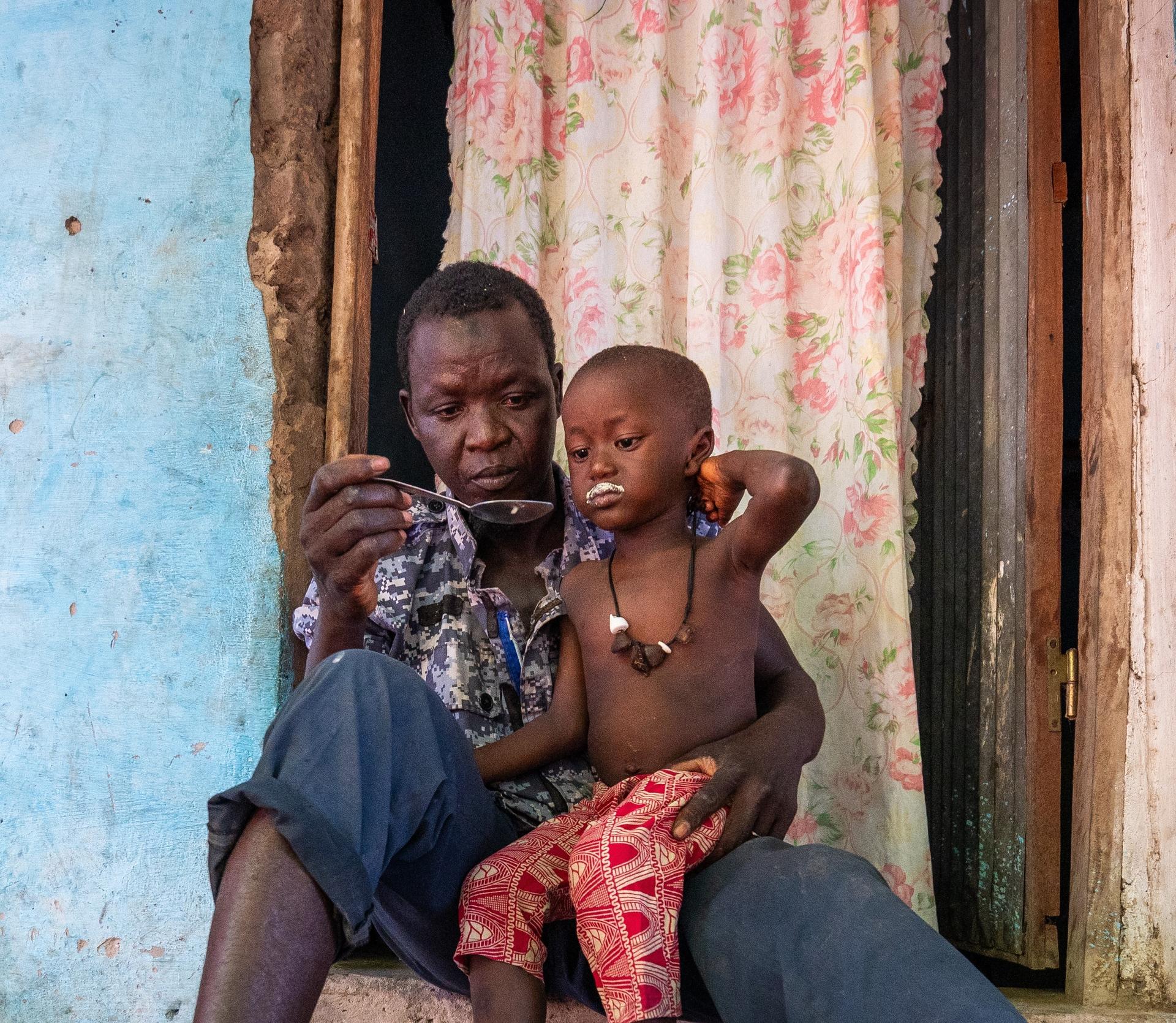 A man sits with a child on his lap, both looking intently at a phone, in a cozy interior.