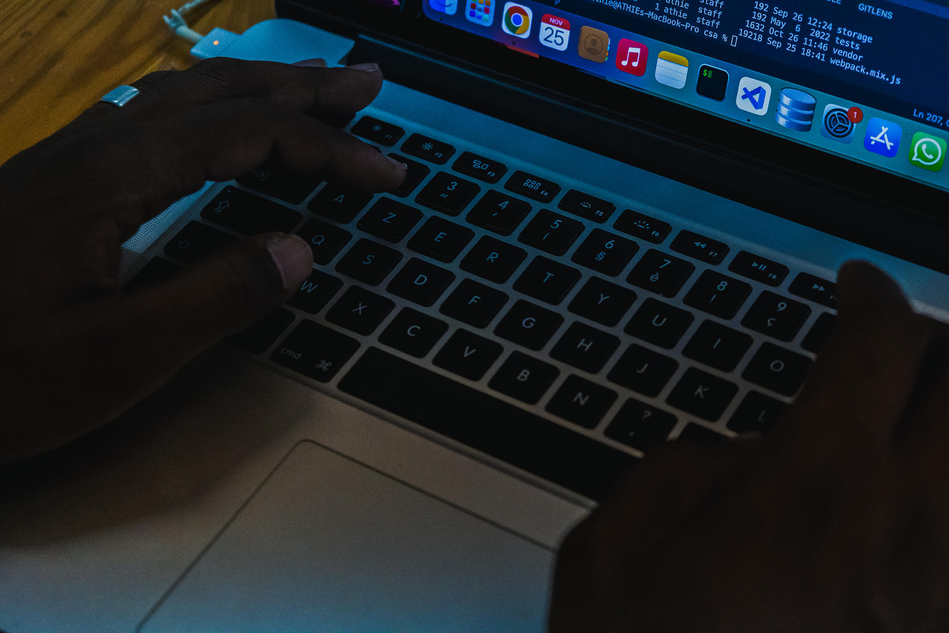 Hands typing on a laptop keyboard, illuminated in dim lighting.