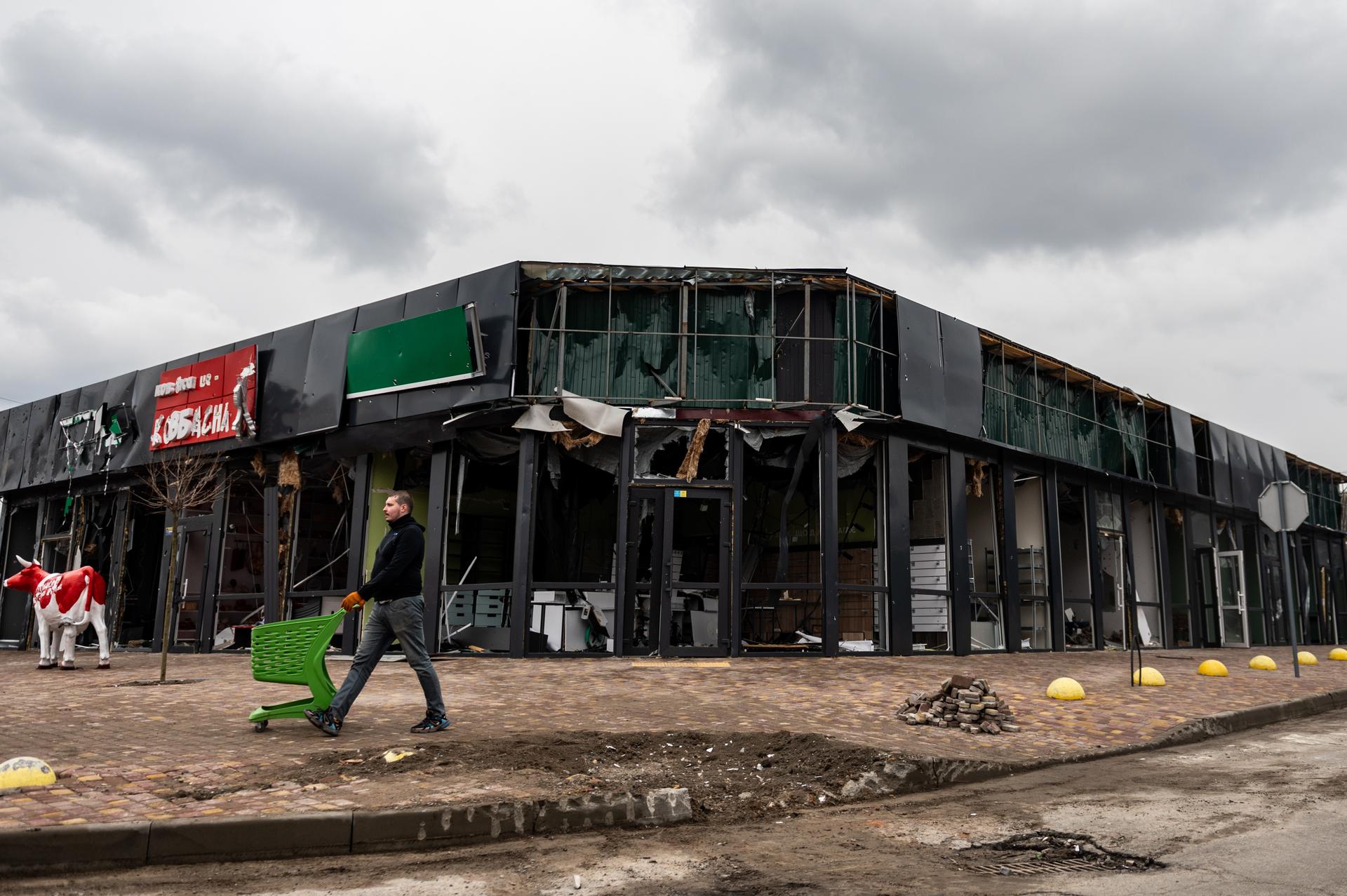 Damaged storefront with exposed walls and a person walking by under cloudy skies.