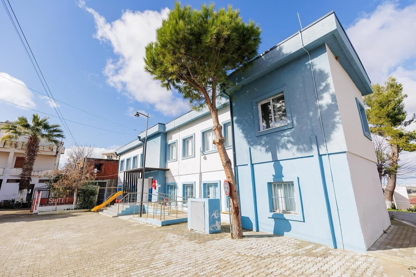 Modern blue and white building with a tree, playground equipment, and clear blue sky.