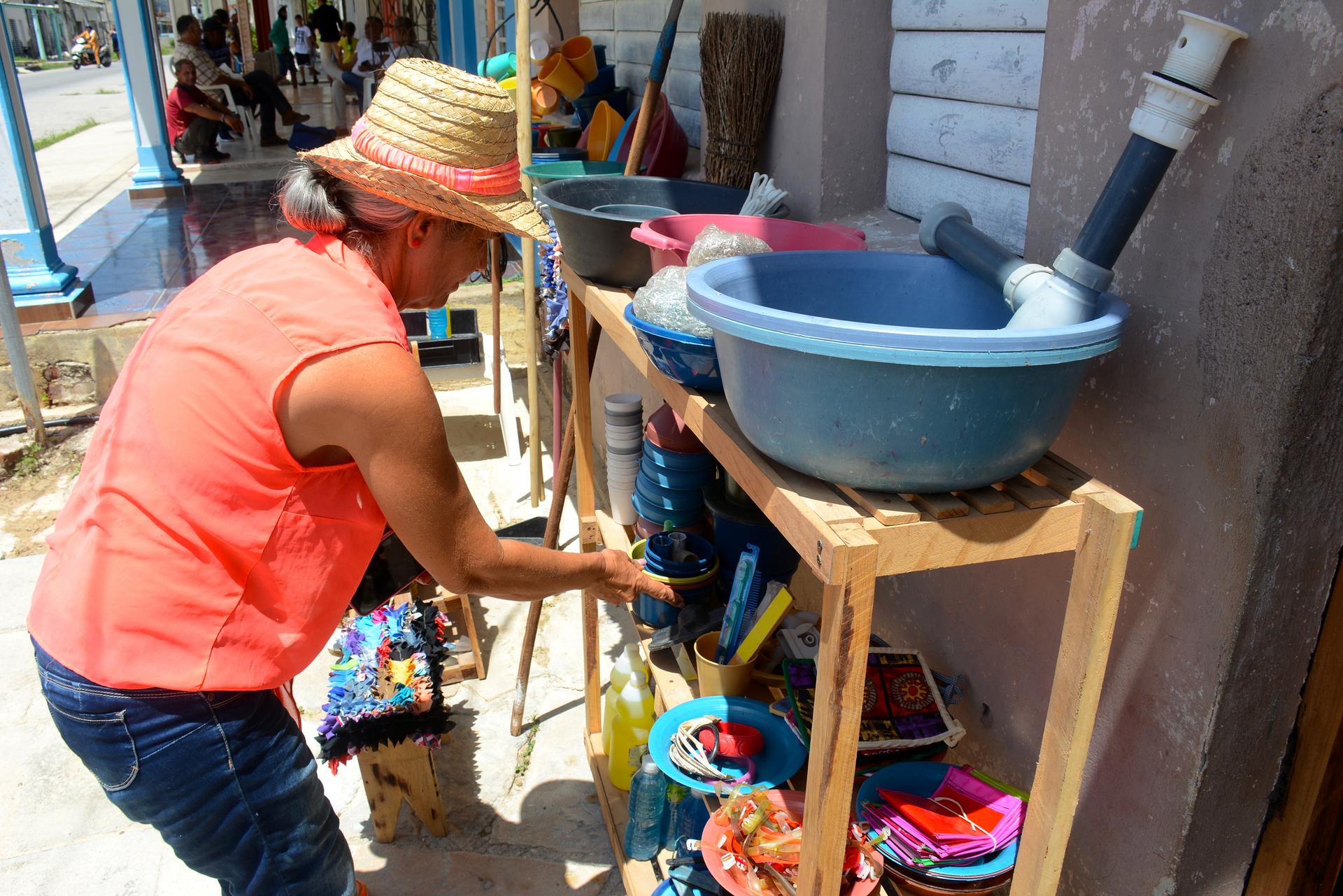 A person in a straw hat organizes colorful items on wooden shelves outdoors.
