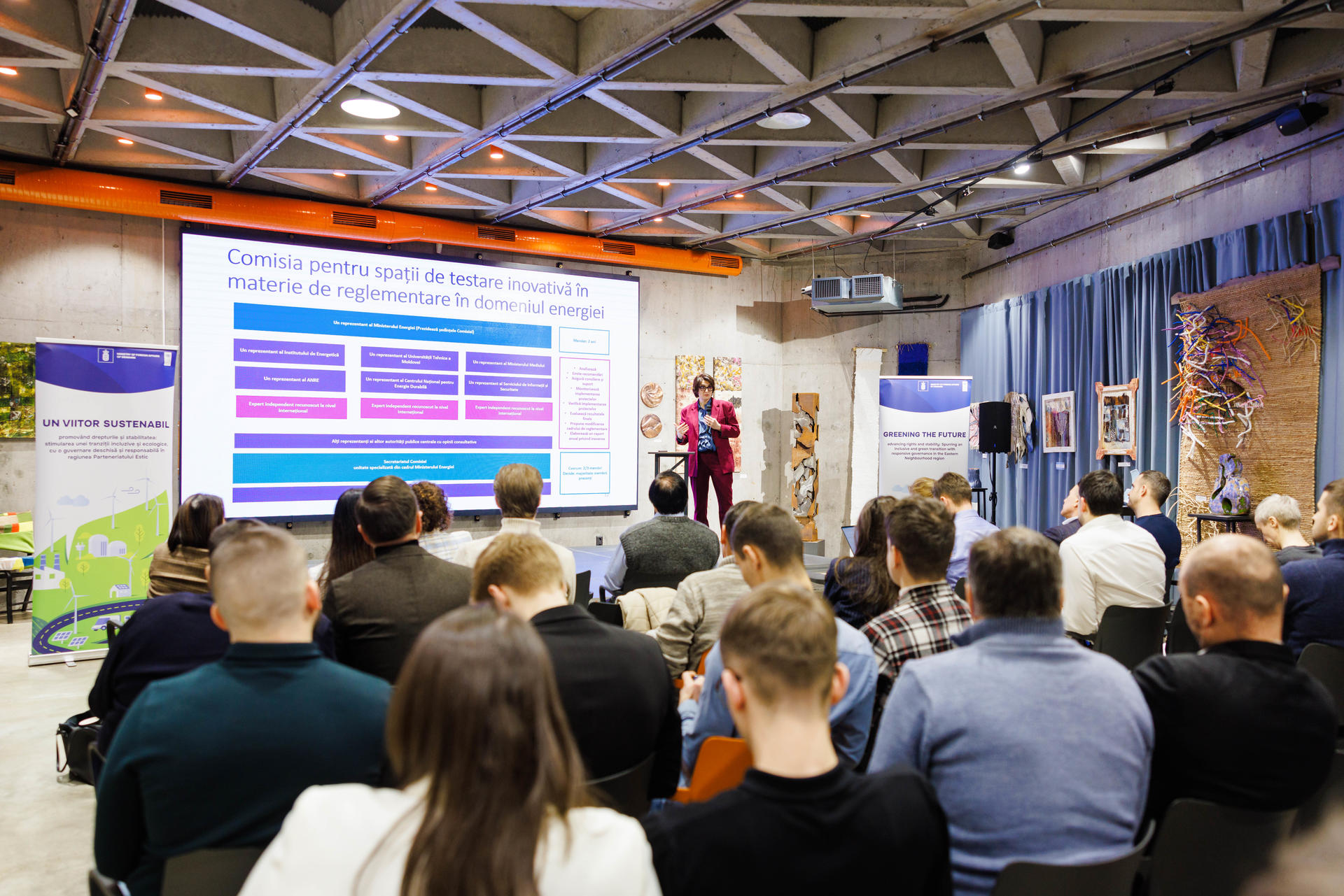 Audience watching a presentation on a large screen in a modern conference setting.