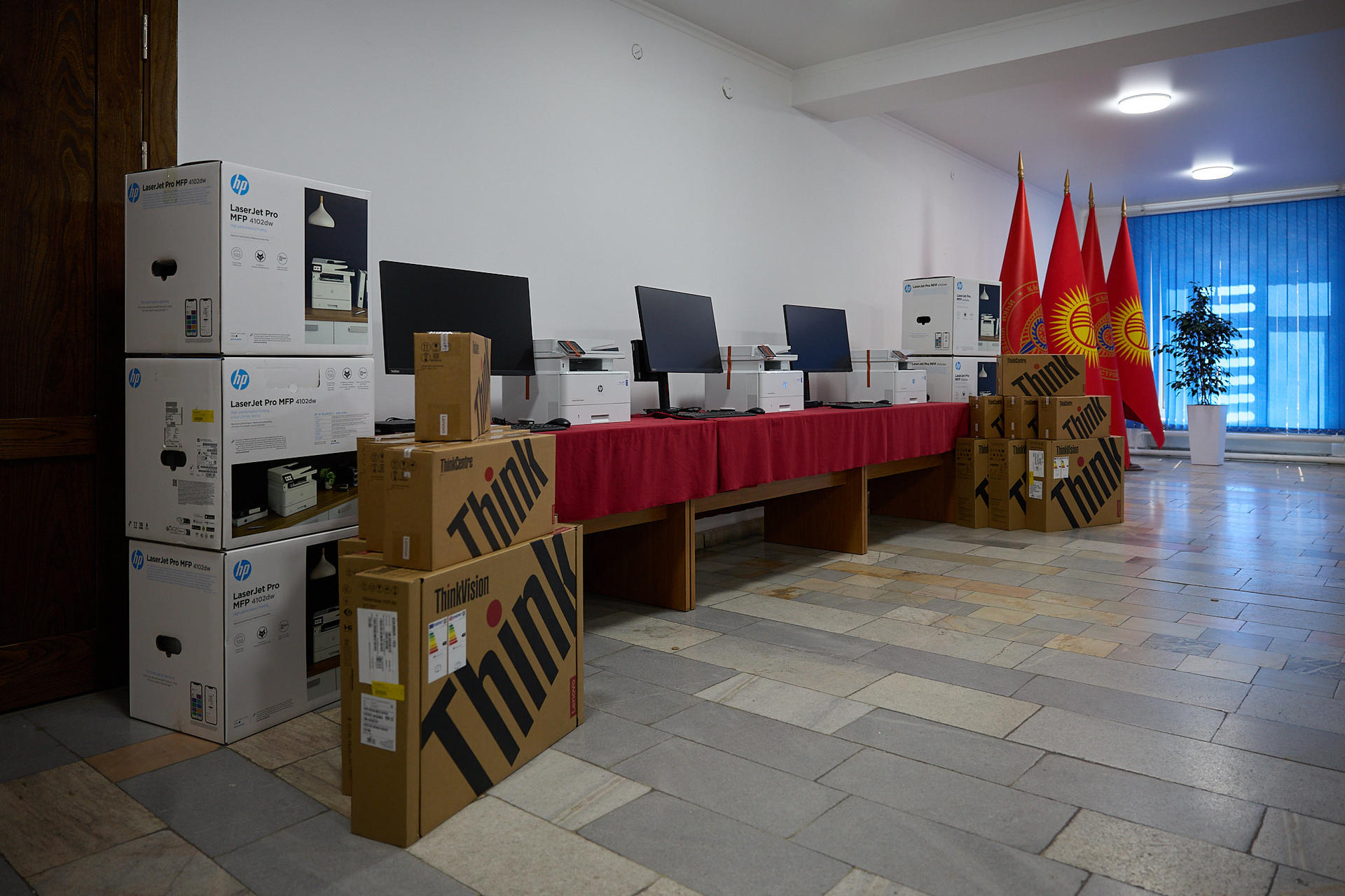 A room displaying several computers on a table, surrounded by flags and cardboard boxes.