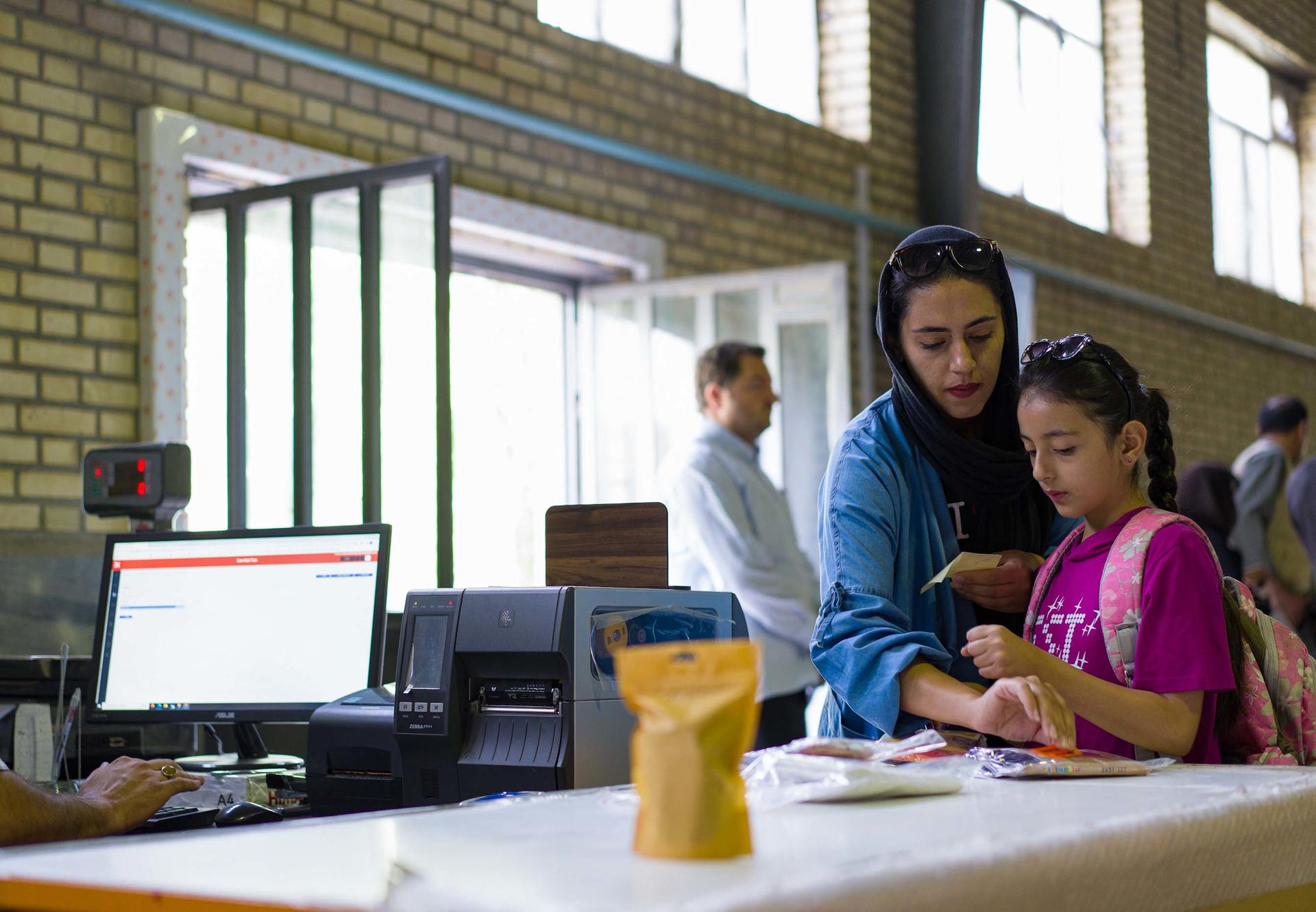 A woman and a girl interact at a service counter in a bright, open space.