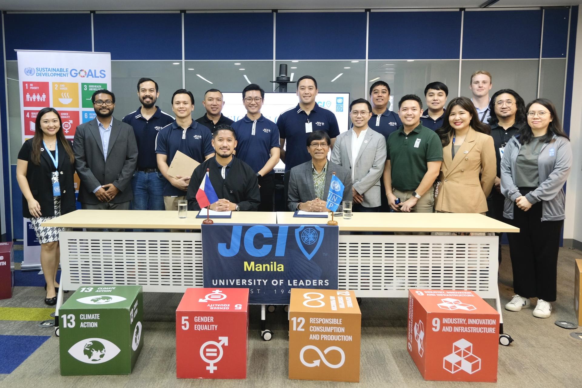 Group photo of people standing behind a table with JCI Manila logo and colorful blocks representing goals.
