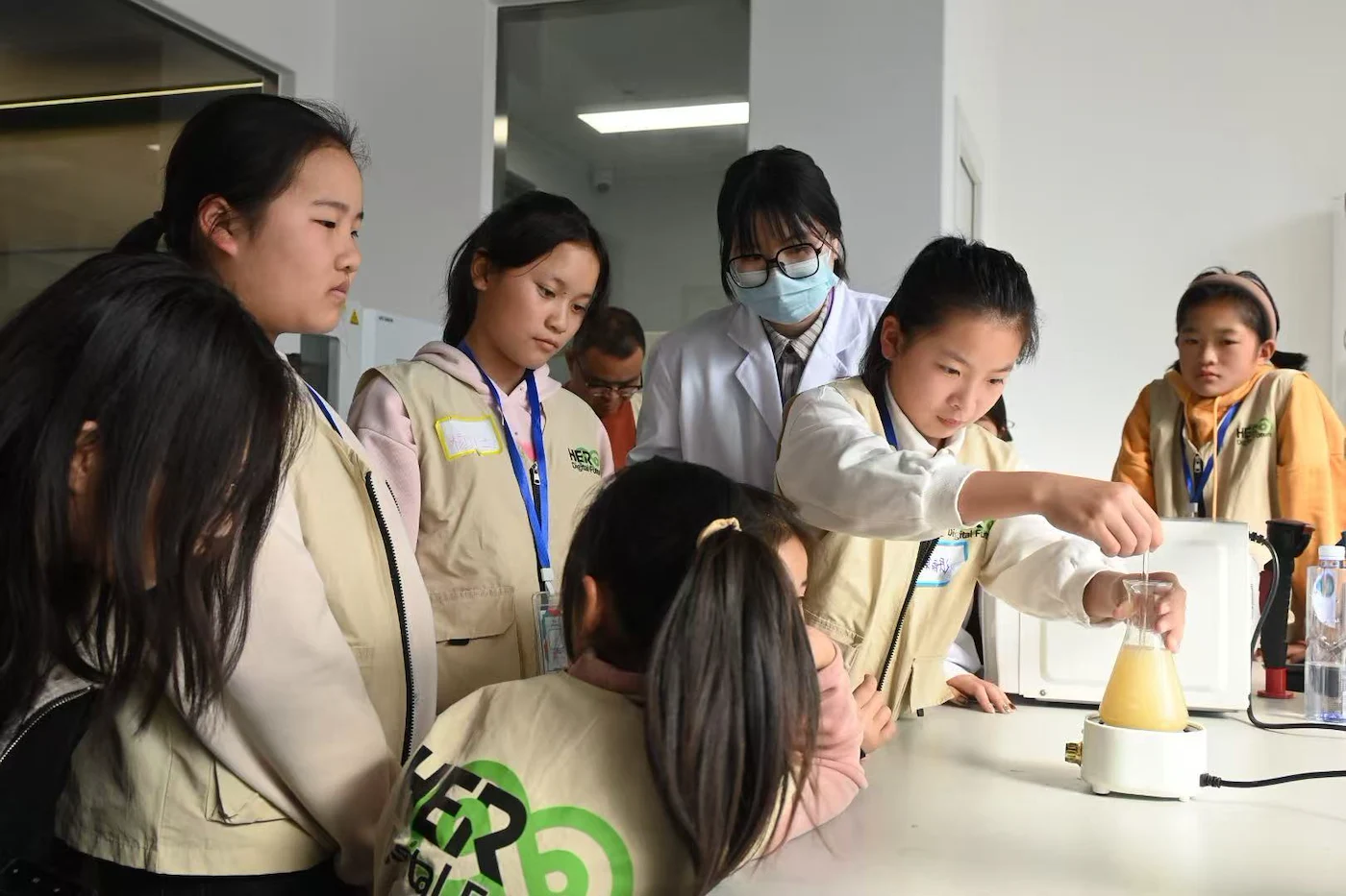 A group of young girls observes a scientist demonstrating an experiment in a laboratory.