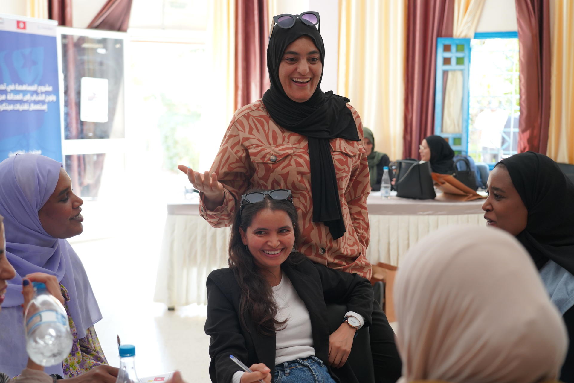 A group of women engaged in discussion in a bright, indoor setting.