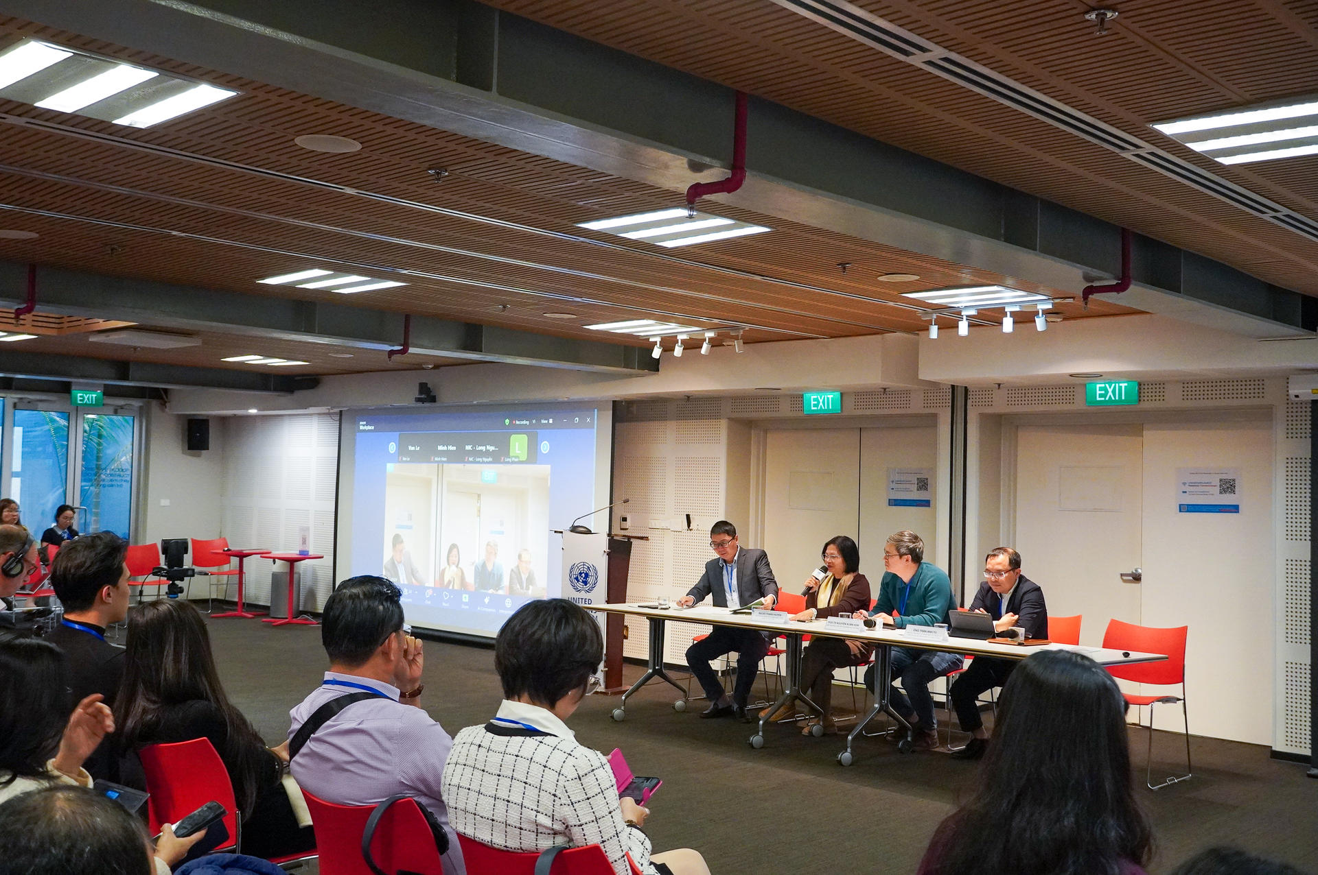 A panel discussion with four speakers at a conference, audience seated in foreground.