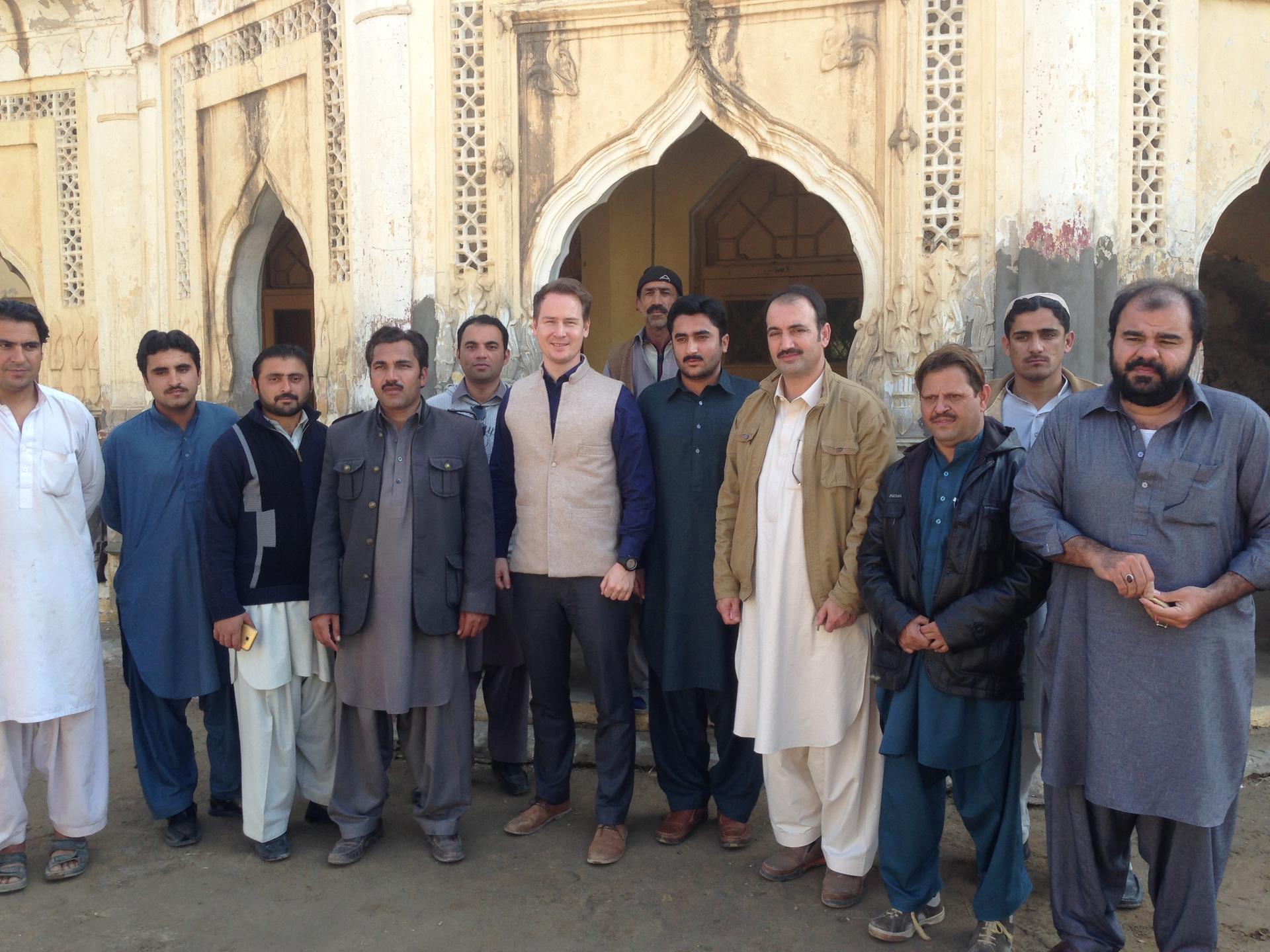 A group of men stands together outside a historic building, smiling for the photograph.